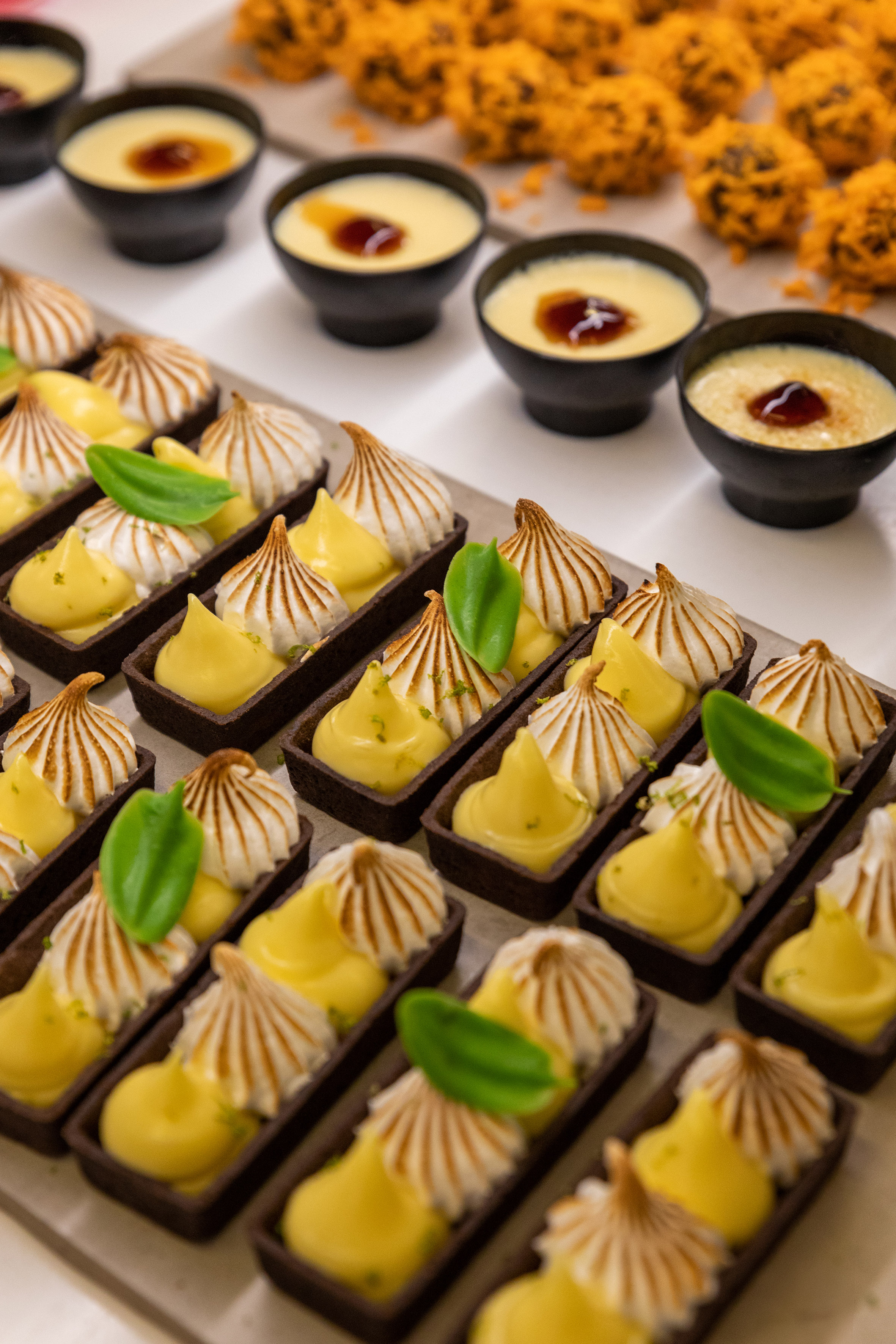 Mini lemon meringue tarts, creamy custards, and crispy orange dessert bites.