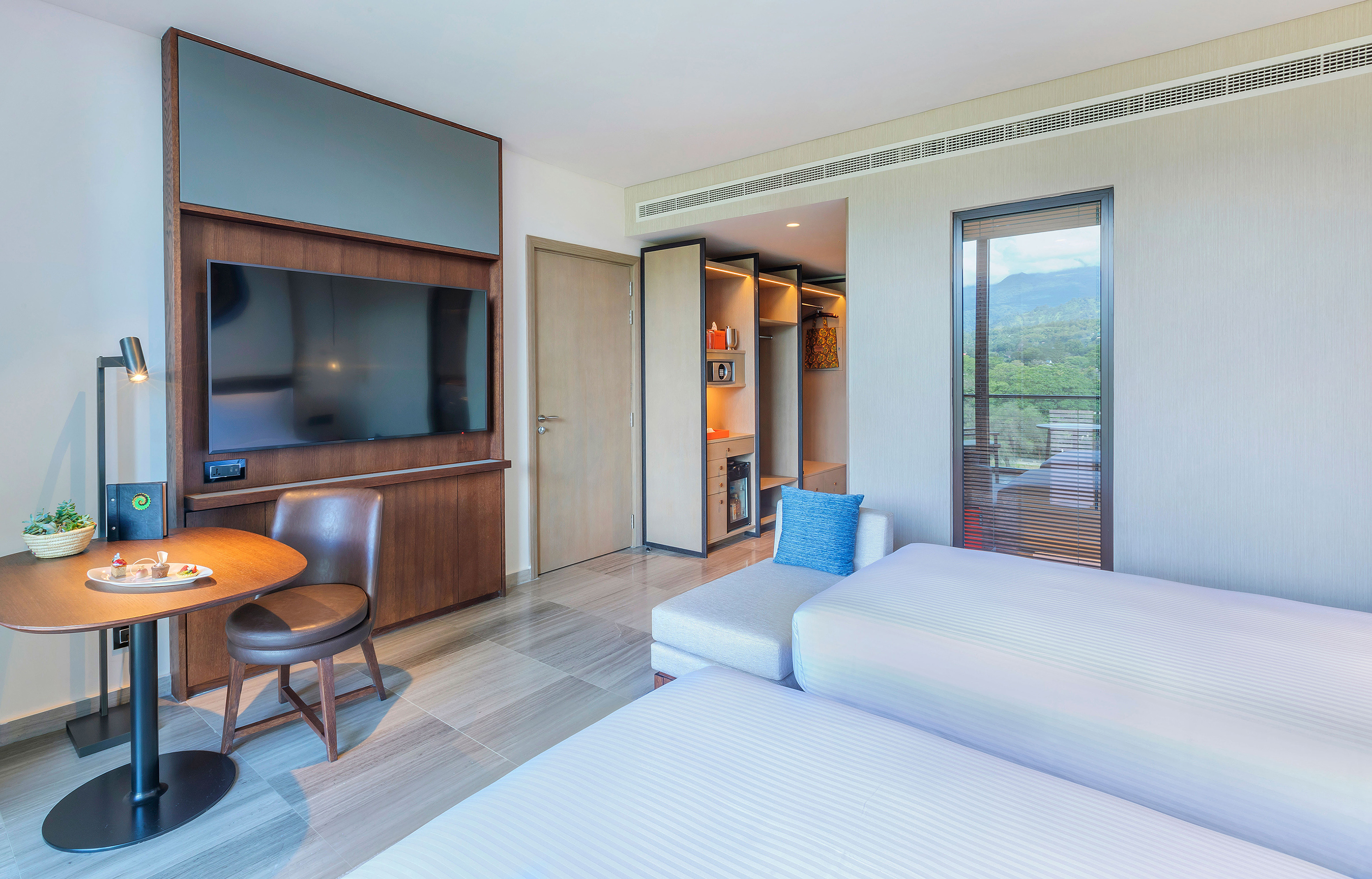 Contemporary hotel room with twin beds, TV, wardrobe, and mountain view.