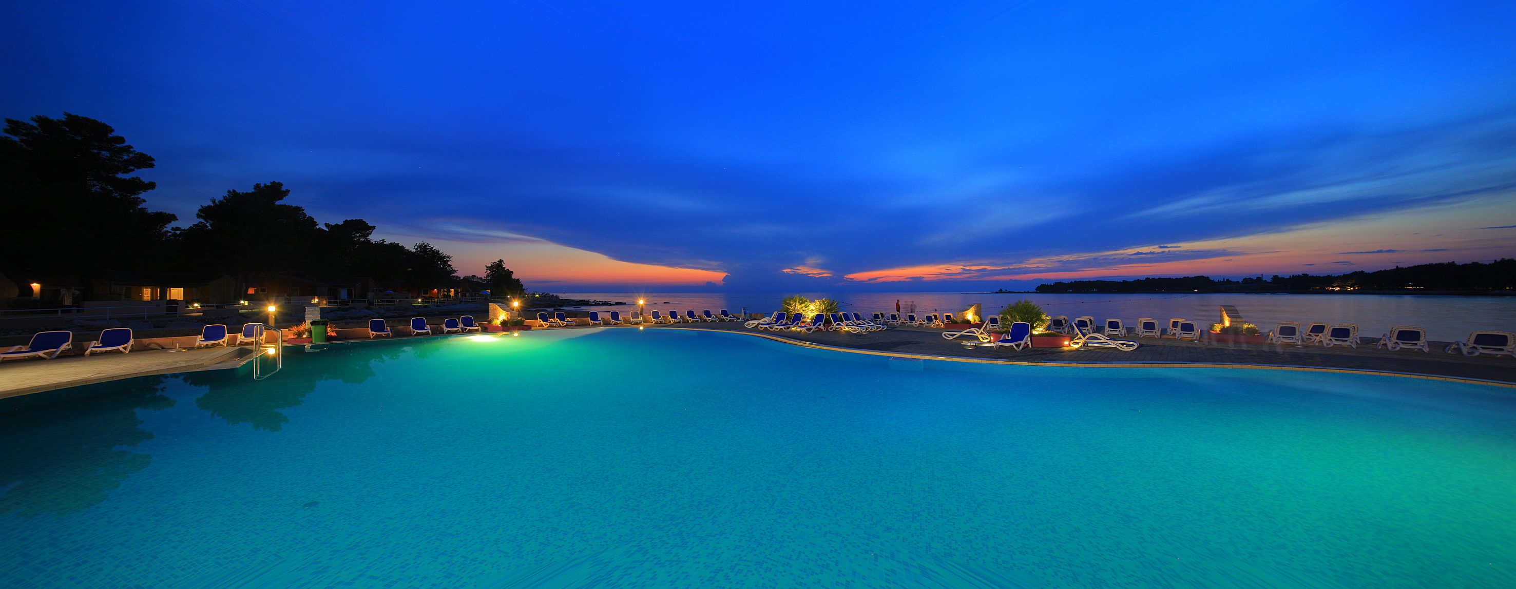 a pool with chairs and lights at sunset