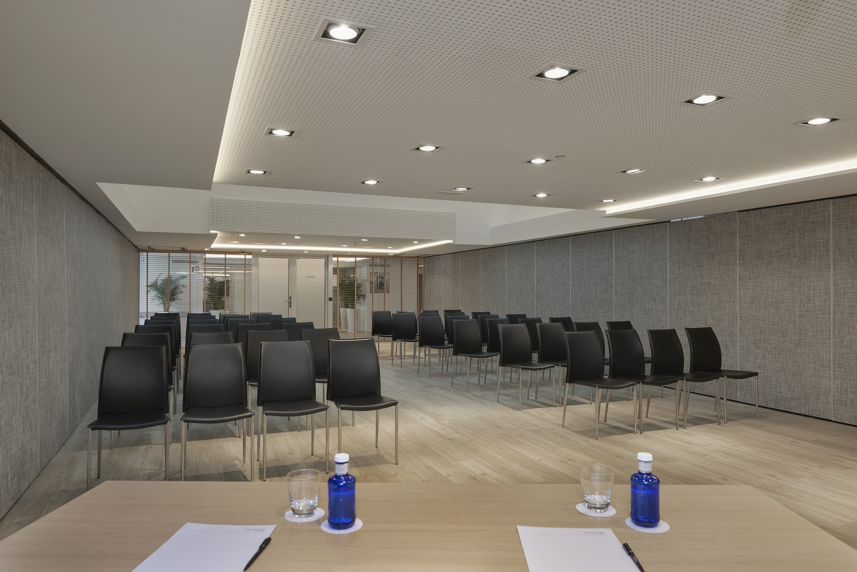 Empty modern conference room with black chairs, wood floor, and ceiling lights.