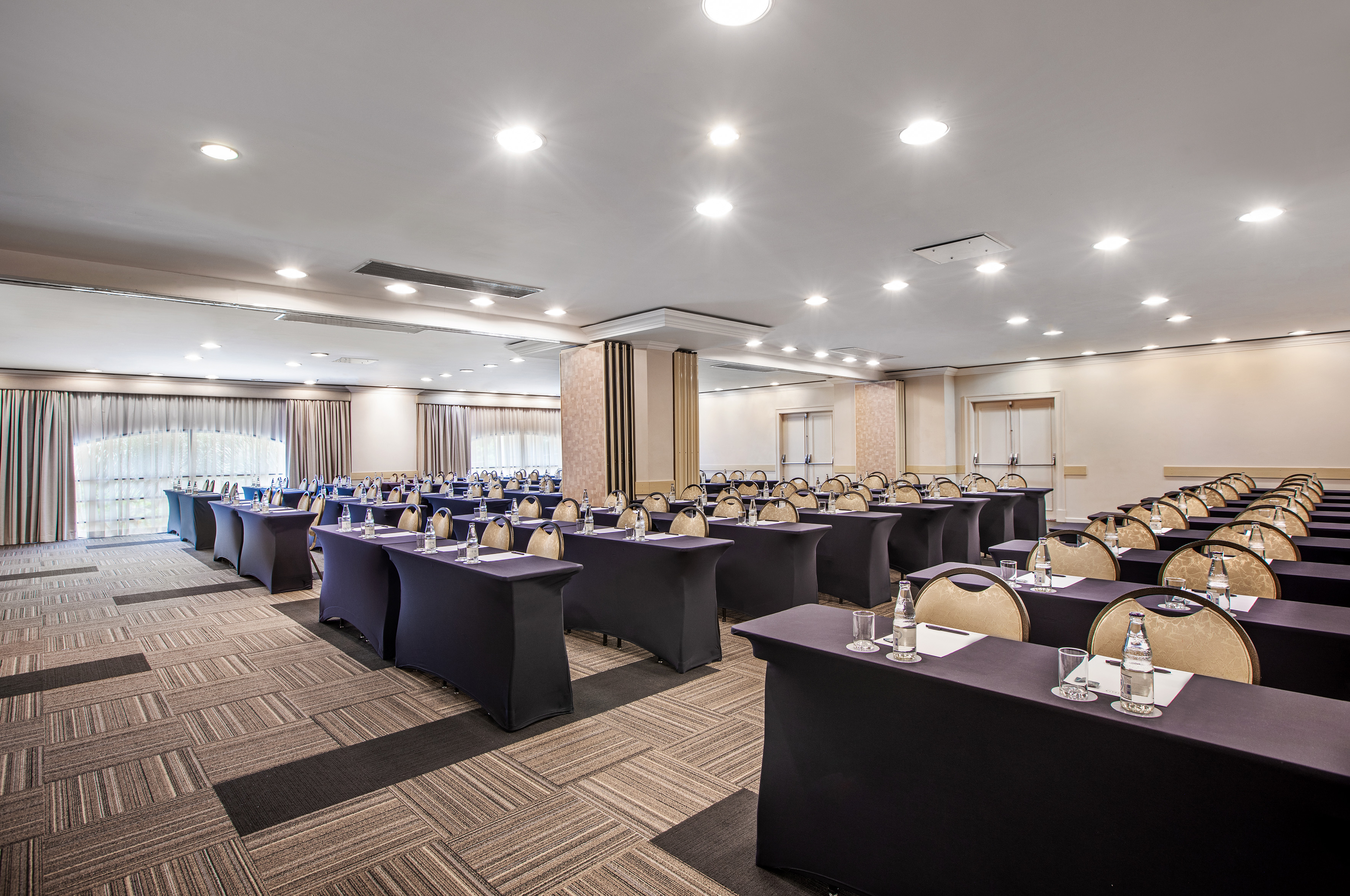 Spacious meeting room with black tables, gold chairs, and water bottles.