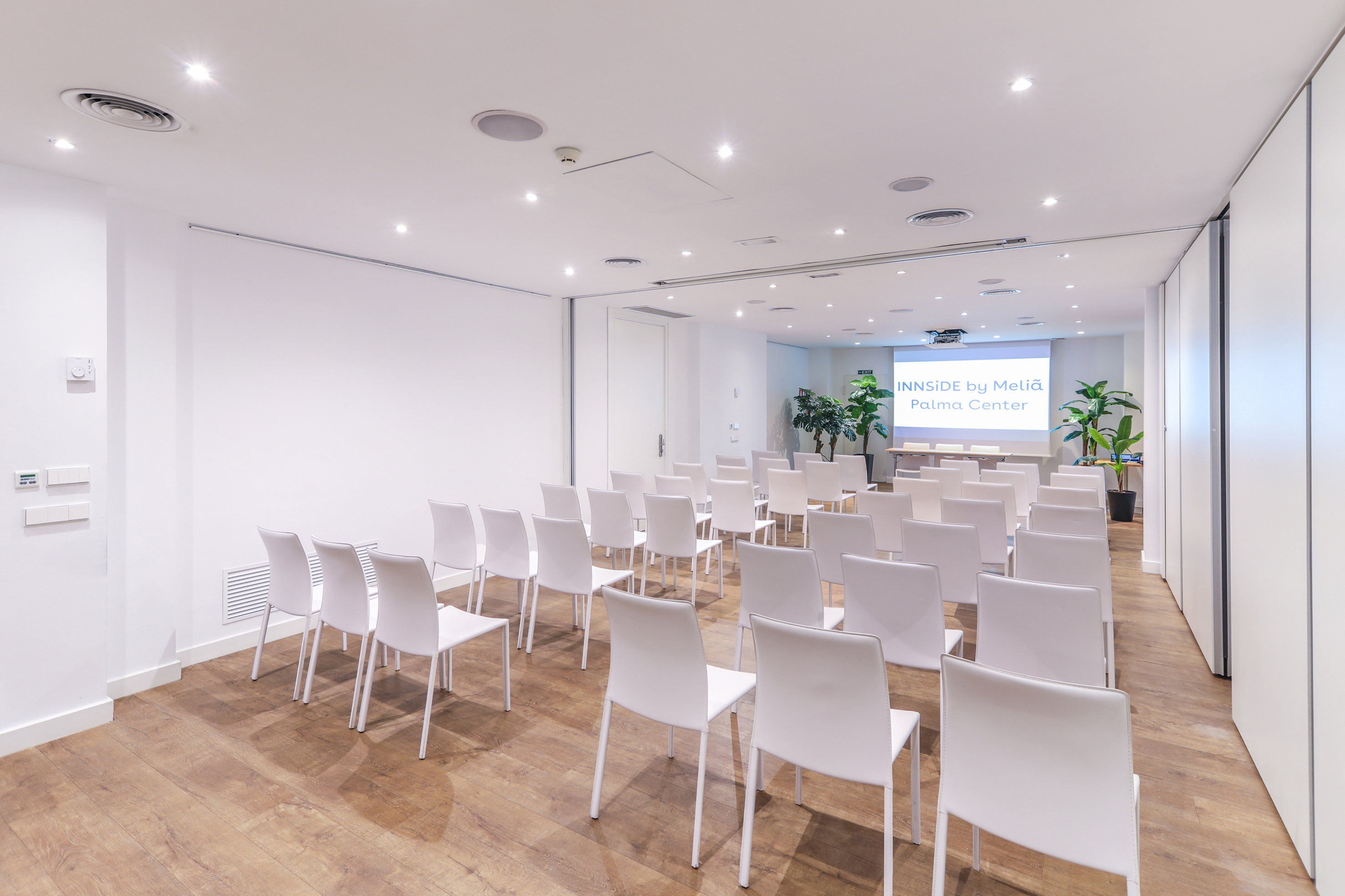 Modern meeting room with white chairs, projector screen, and wood floor.