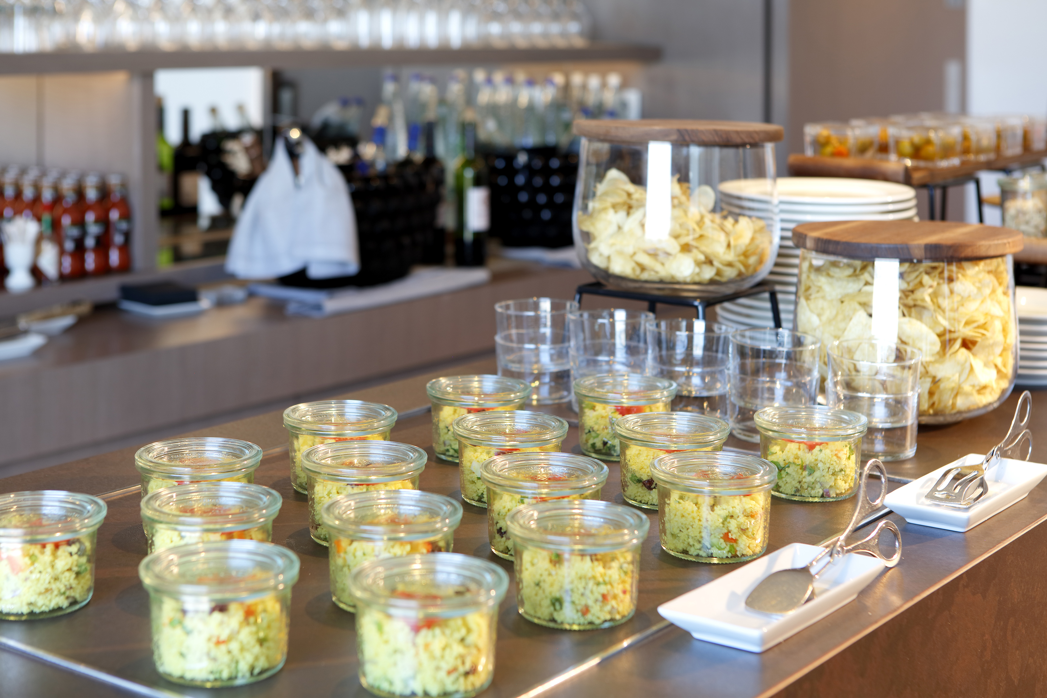 Individual couscous salads and potato chips at a modern buffet spread.