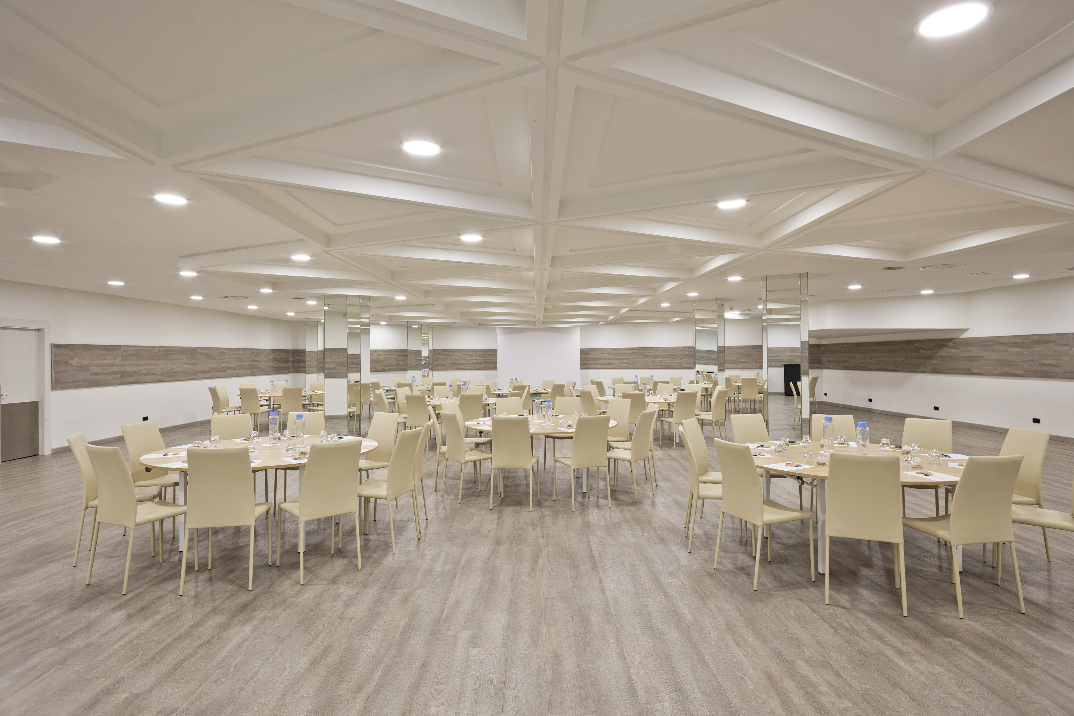 Spacious event hall with multiple round tables, cream chairs, and modern decor.