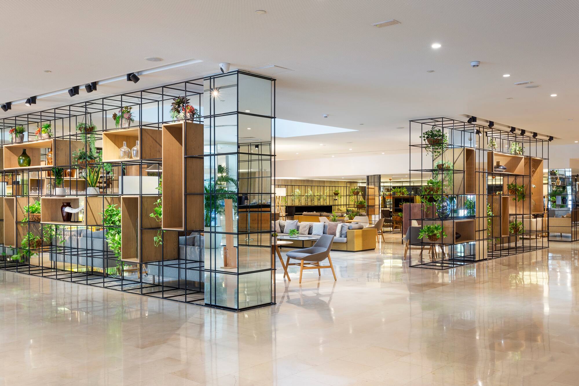 Modern hotel lobby with green plant dividers, lounge seating, and marble floor.