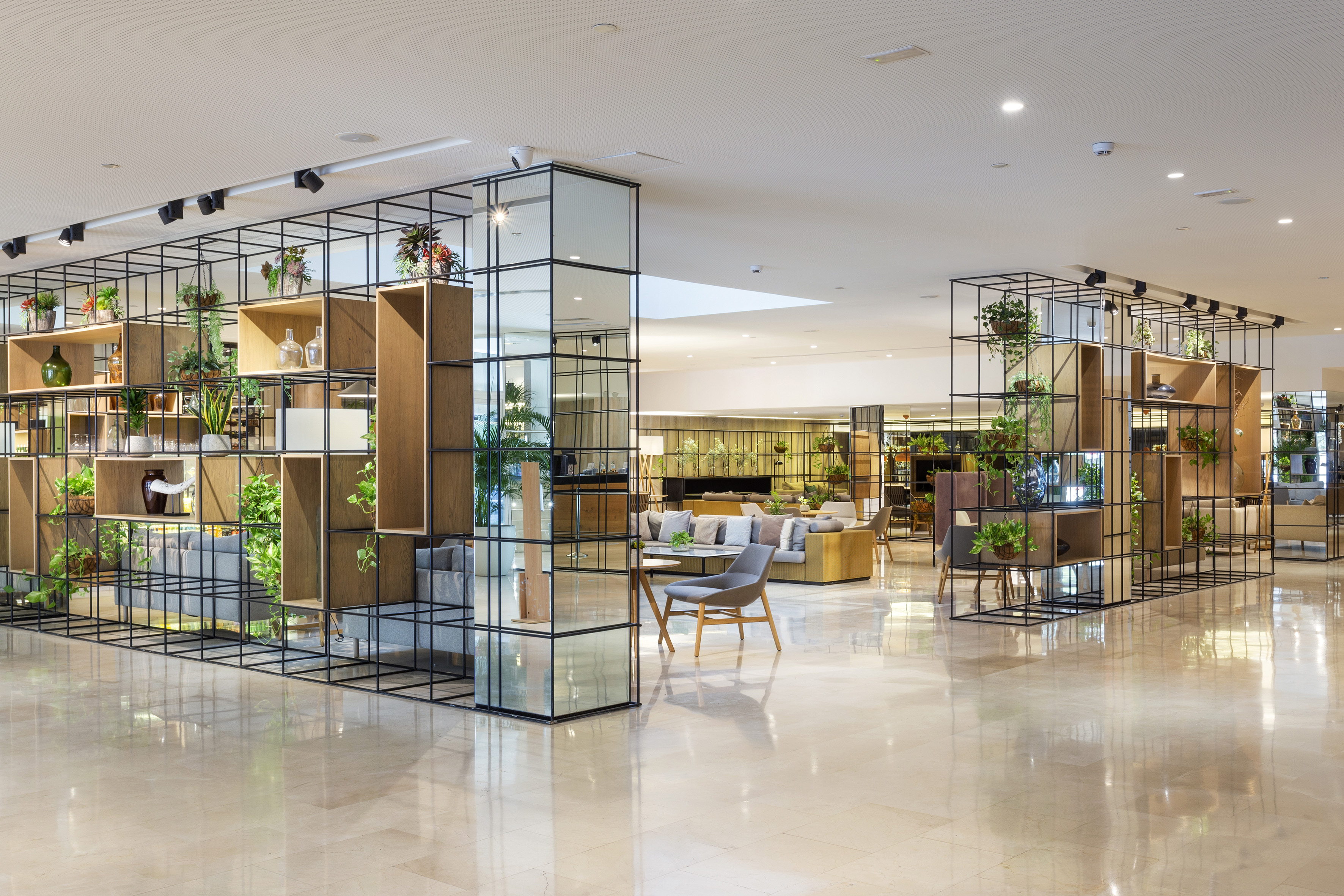 Modern hotel lobby with green plant dividers, lounge seating, and marble floor.