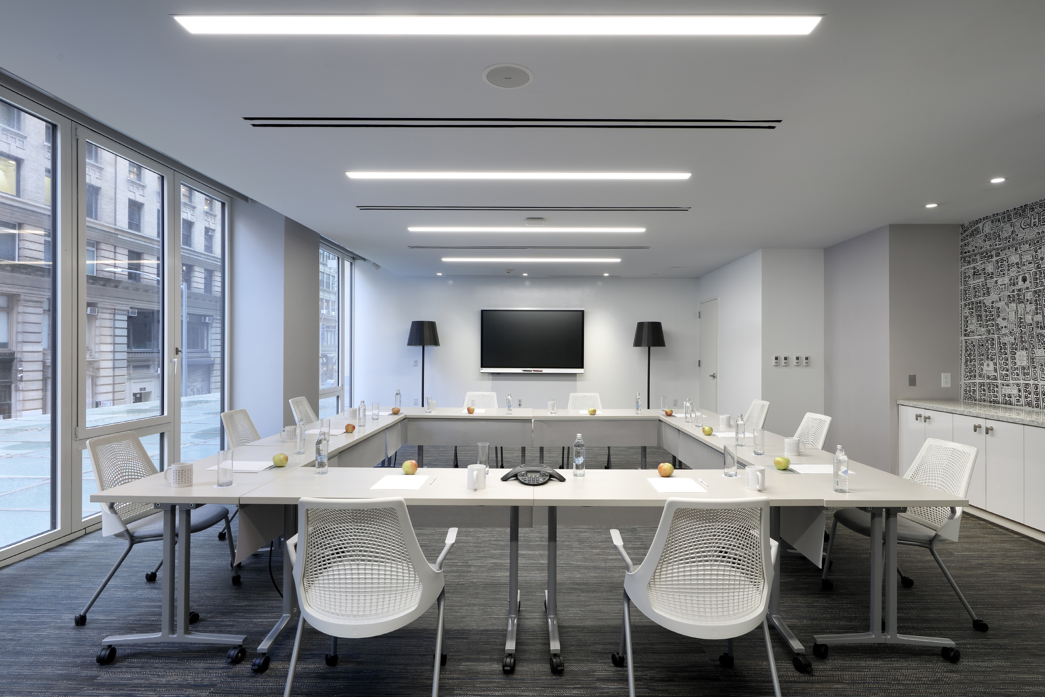 Modern conference room, U-shaped table, white chairs, city windows, wall TV...