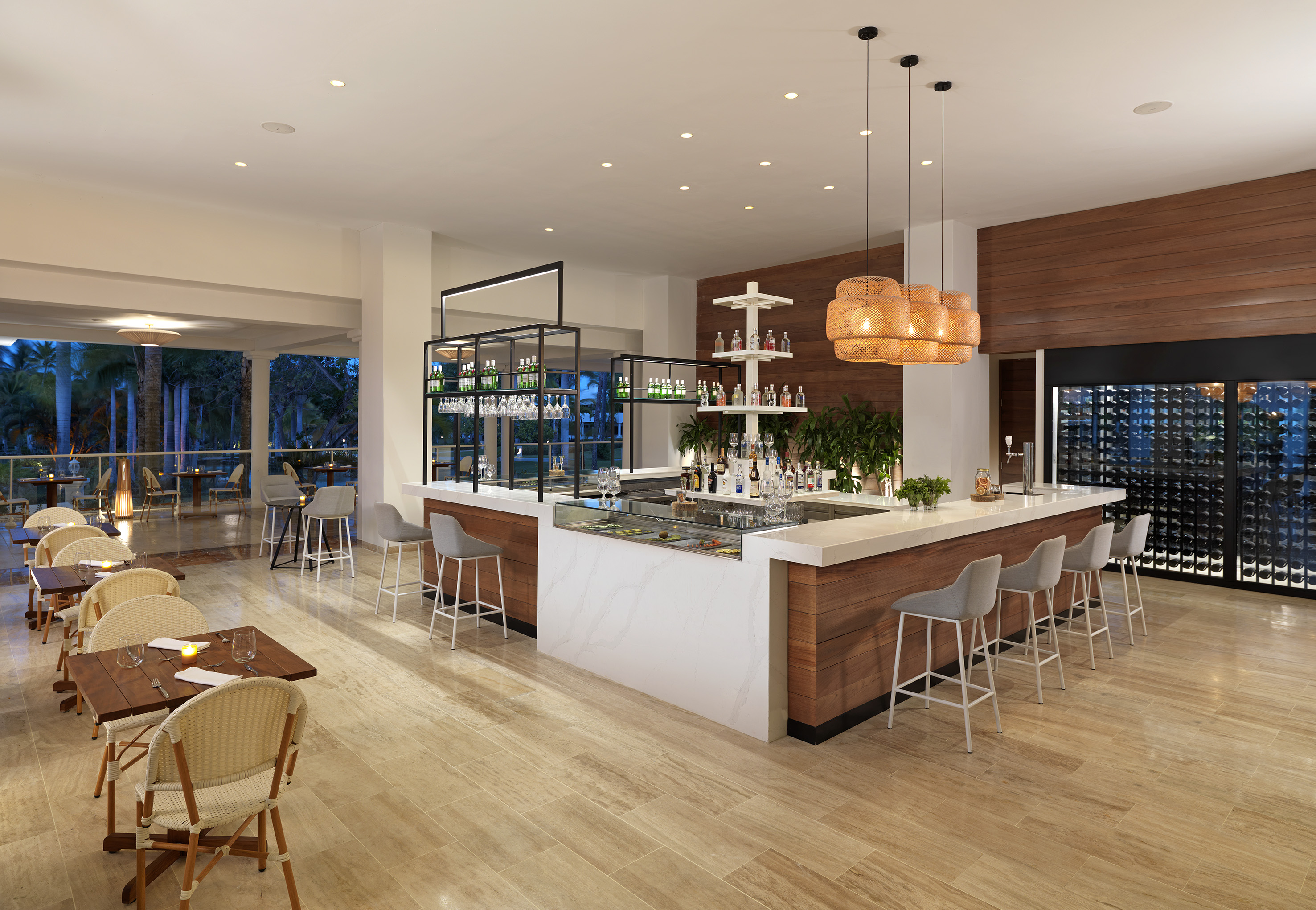 Modern resort bar with marble counter, stools, and outdoor dining tables.