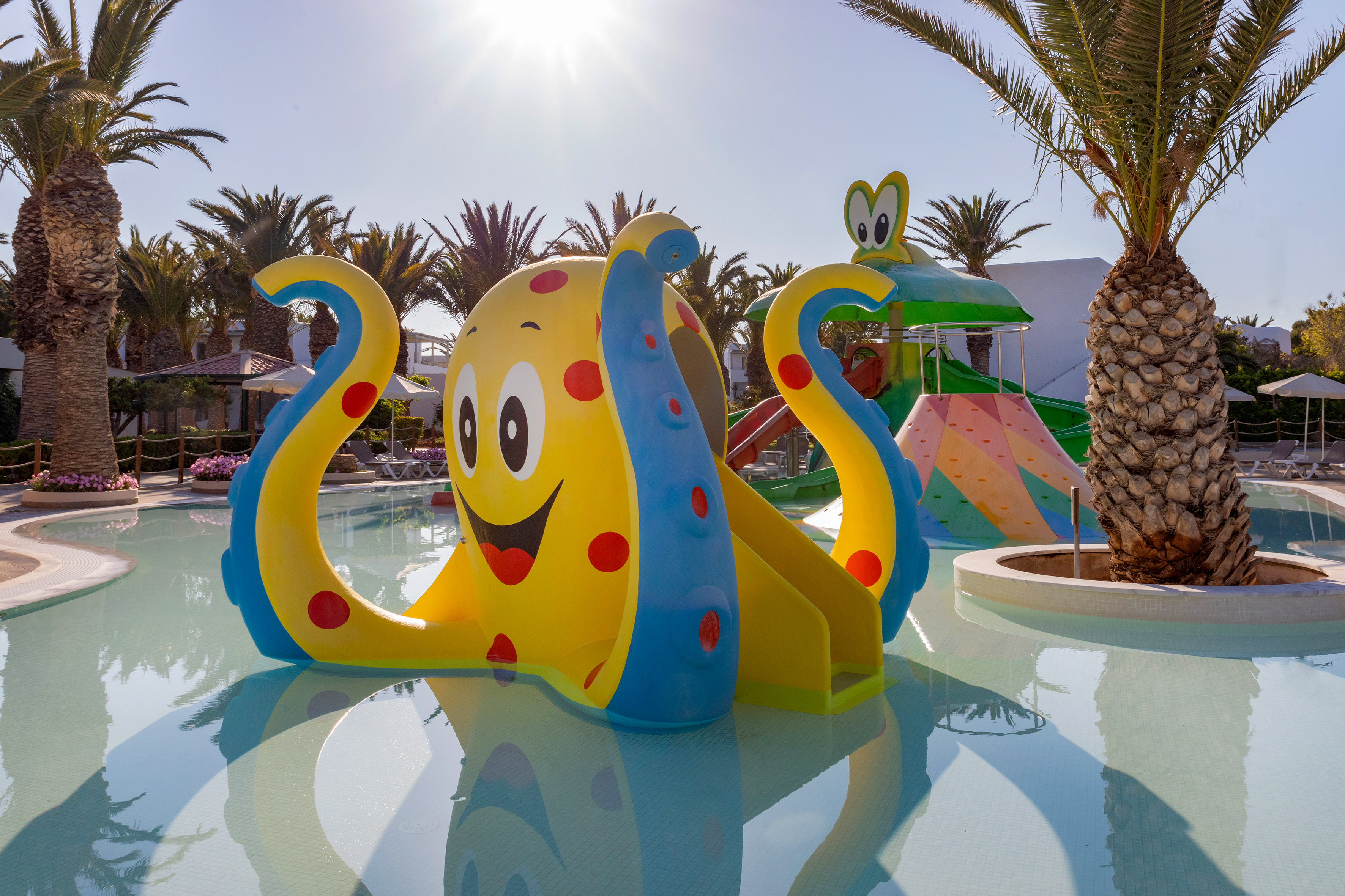 Colorful octopus water slide in resort pool with palm trees.