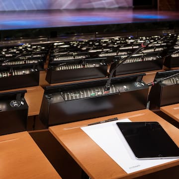 a row of desks with microphones and a tablet on top