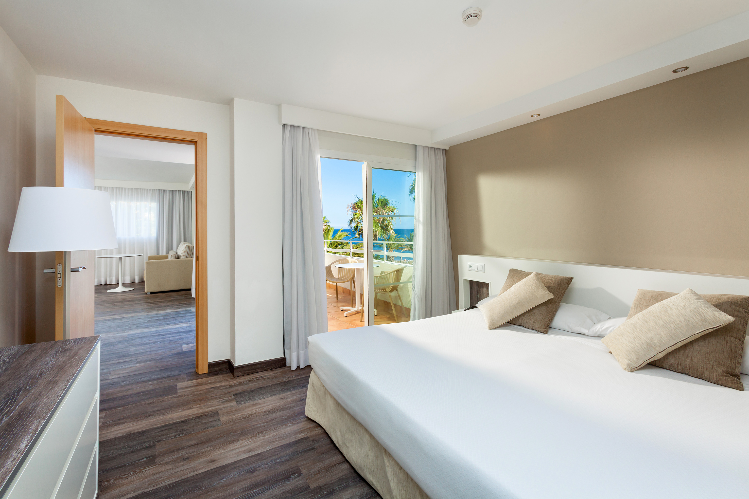 Hotel suite bedroom with ocean view balcony, large bed, and dark wood floor.