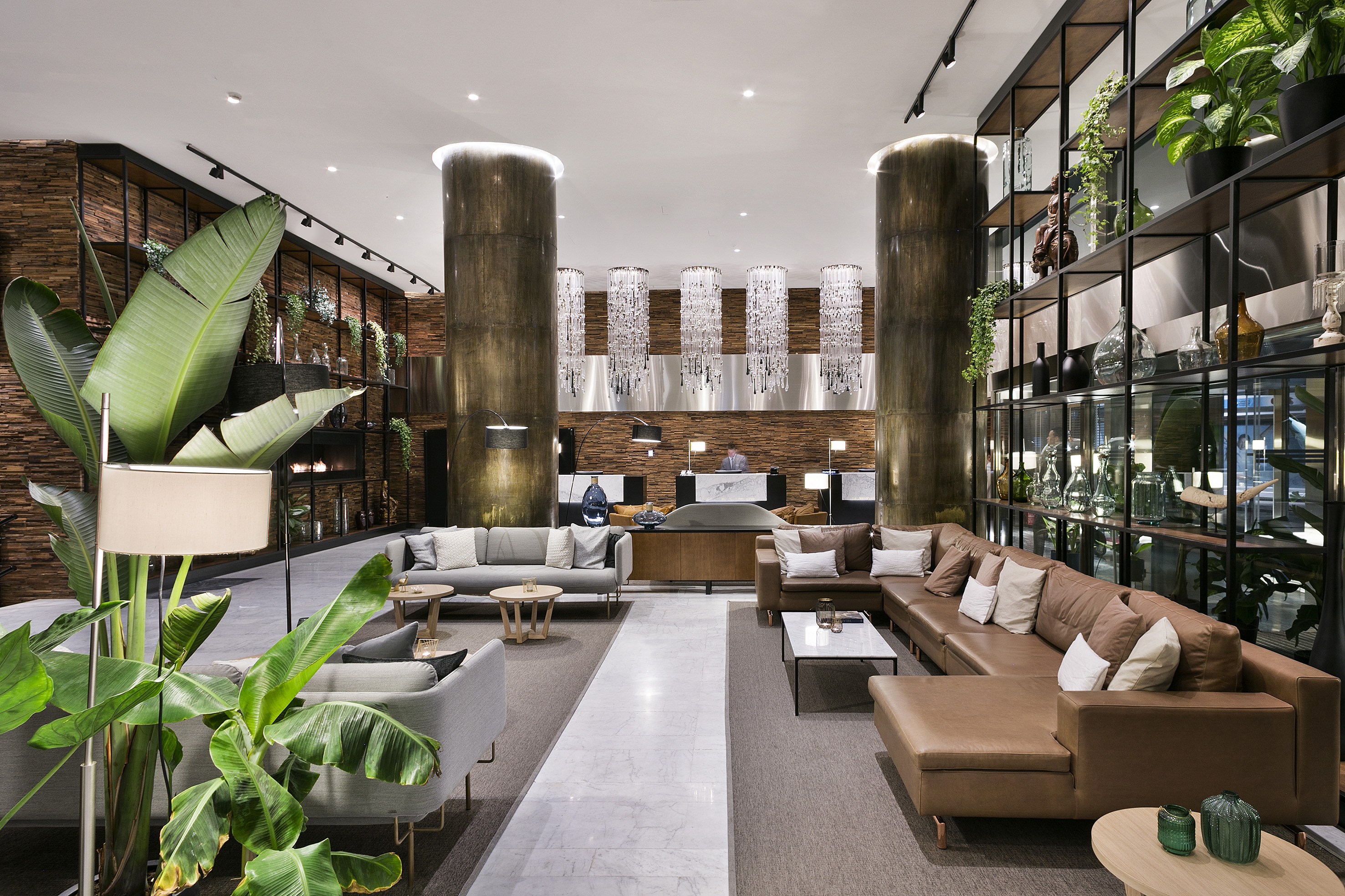 Hotel lobby with modern sofas, large plants, reception area, and chandeliers.