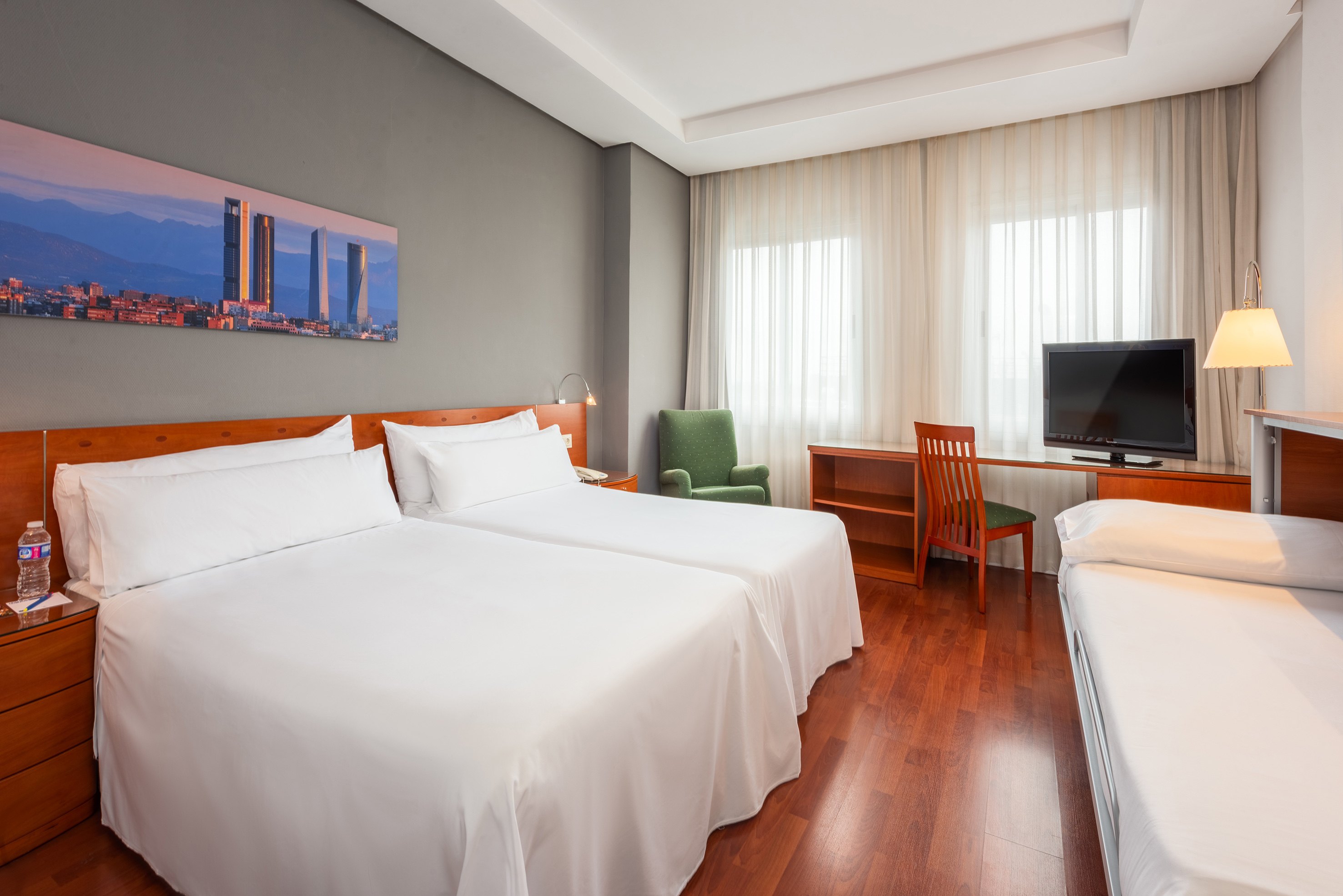 Hotel family room with twin beds, extra bed, desk, TV, and city art.