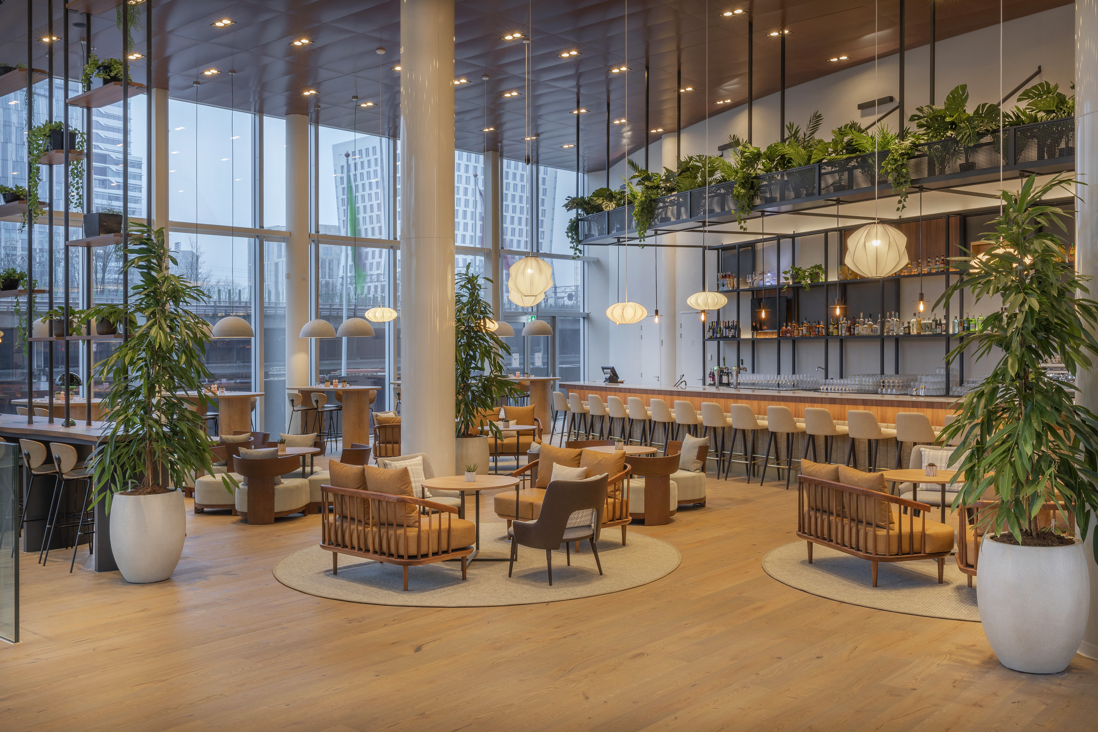 Modern lounge bar with large windows, lush plants, and contemporary seating.
