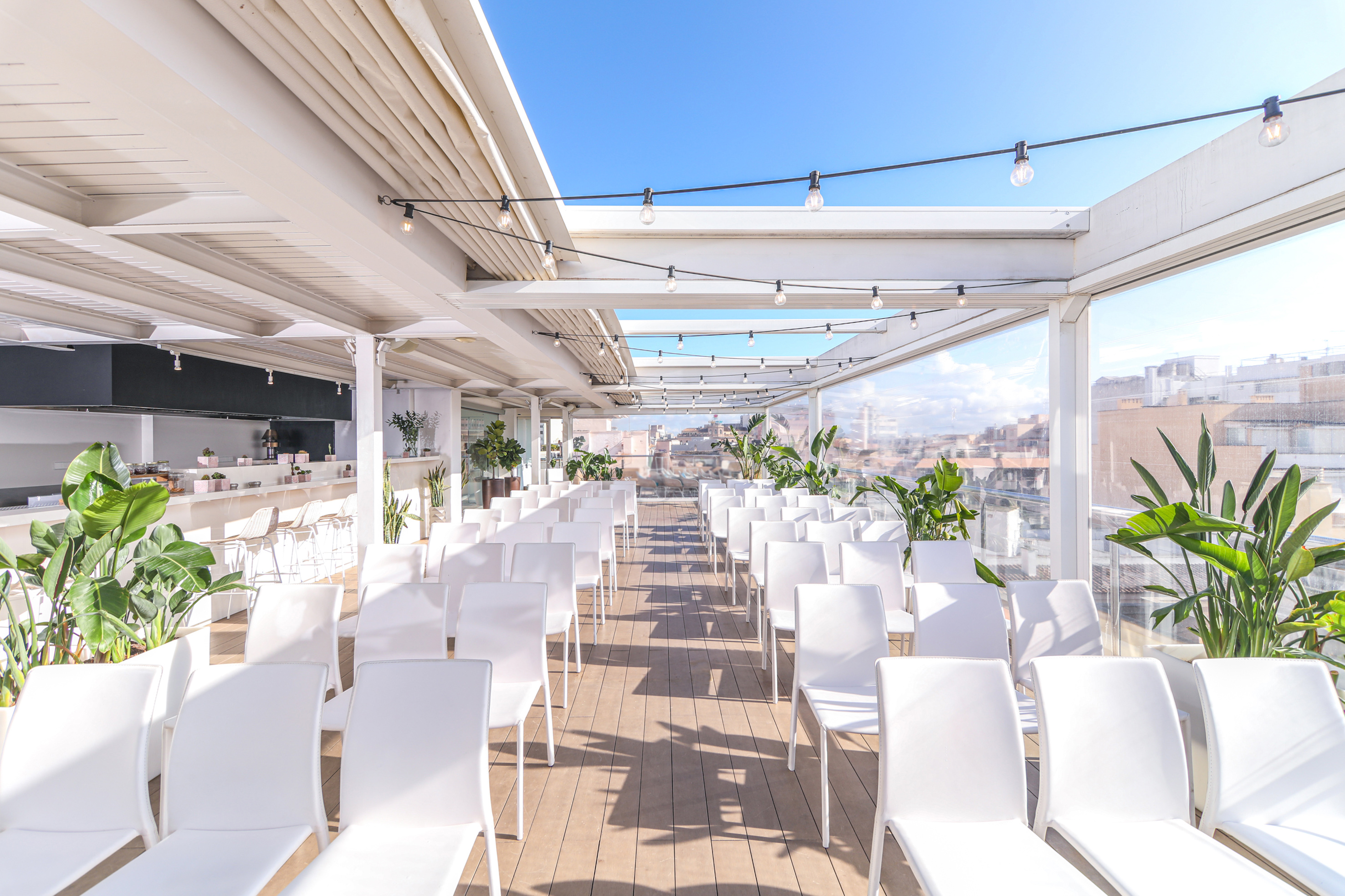 Rooftop event venue with white chairs, string lights, and city view.