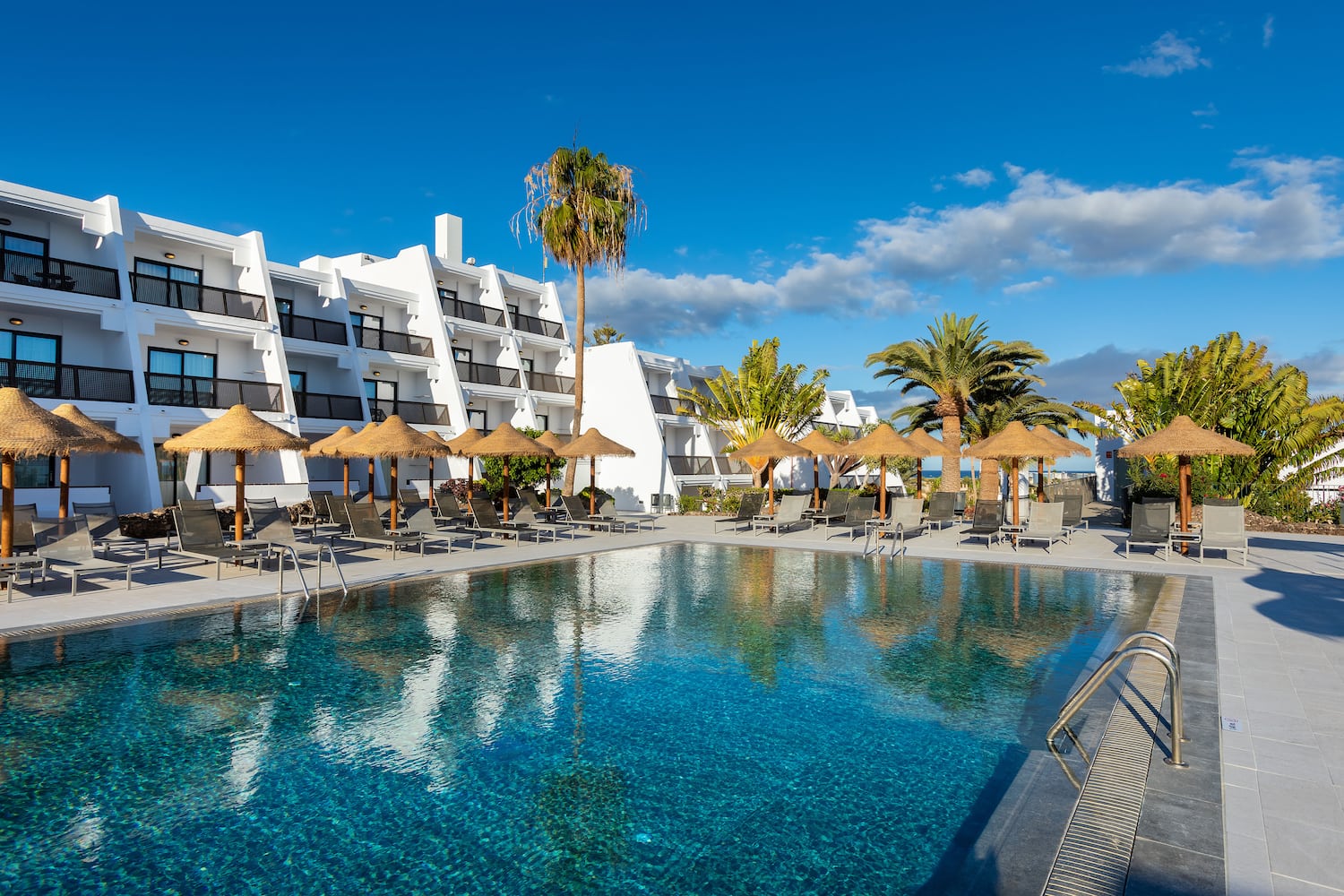 a pool with umbrellas and chairs in front of a building