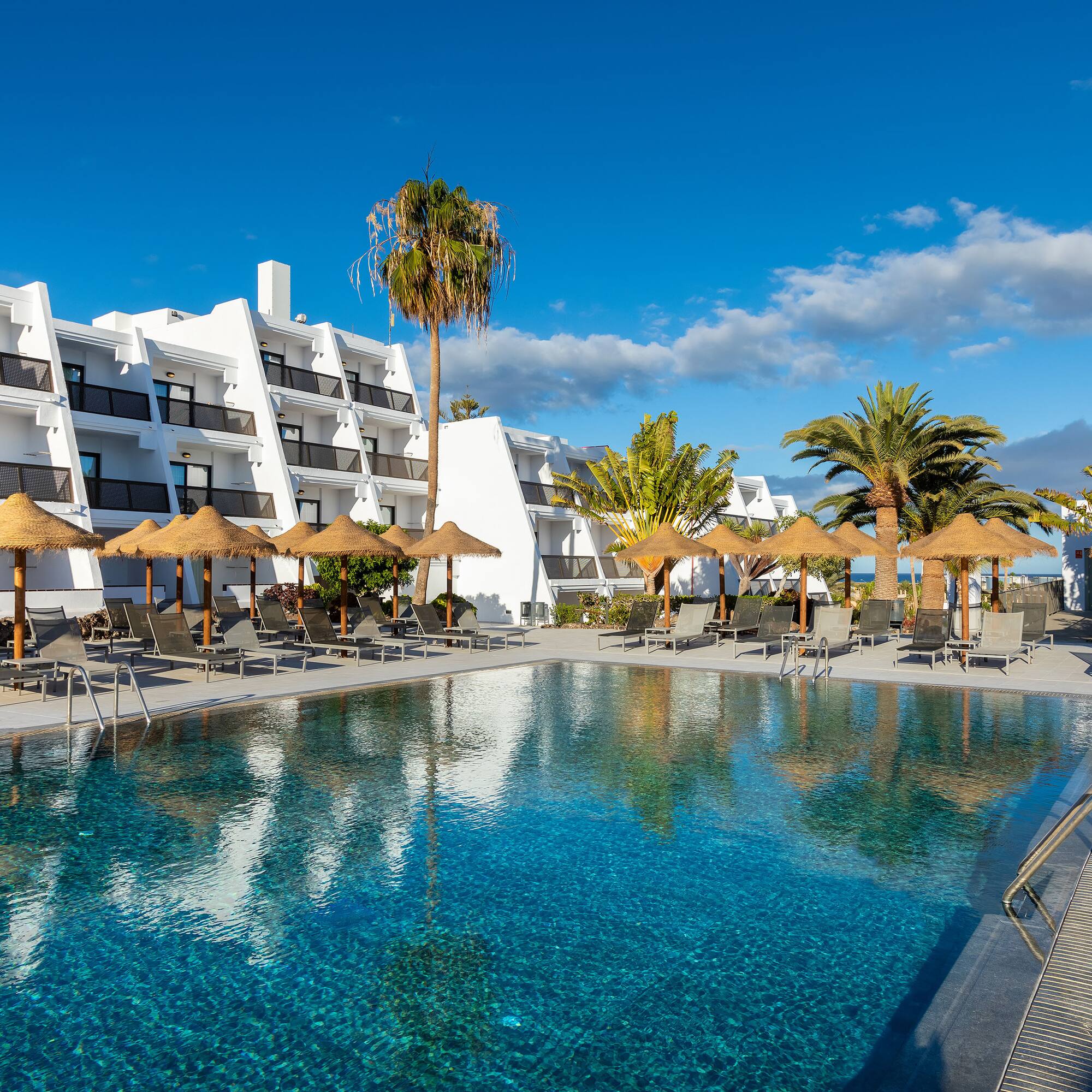 a pool with umbrellas and chairs in front of a building
