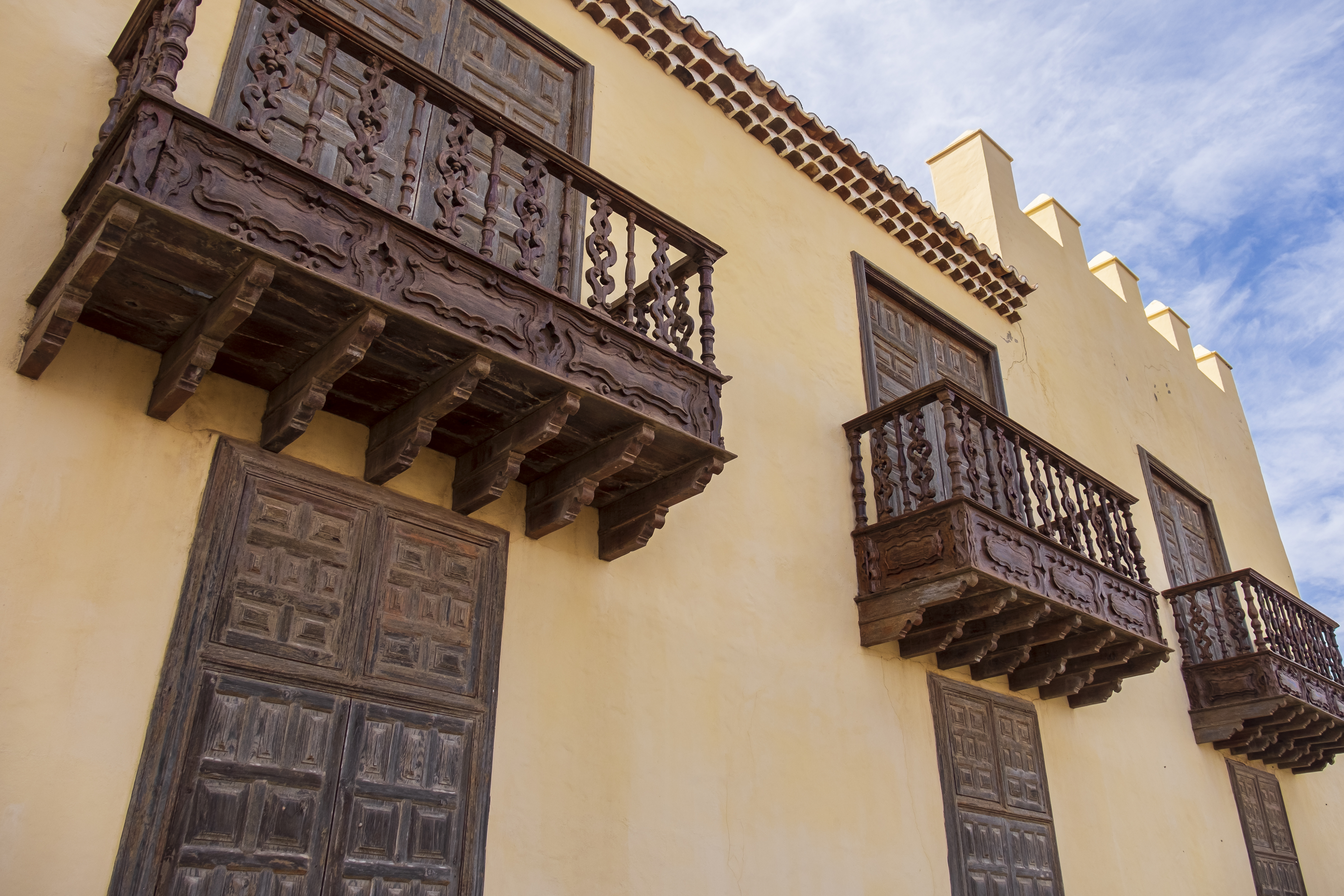 Ornate carved dark wood balconies on a traditional yellow stucco building.