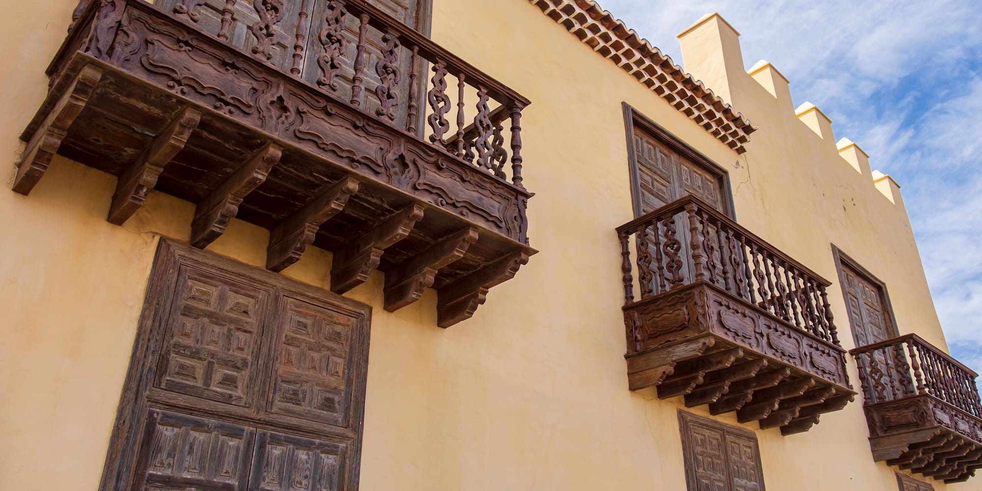 Ornate carved dark wood balconies on a traditional yellow stucco building.