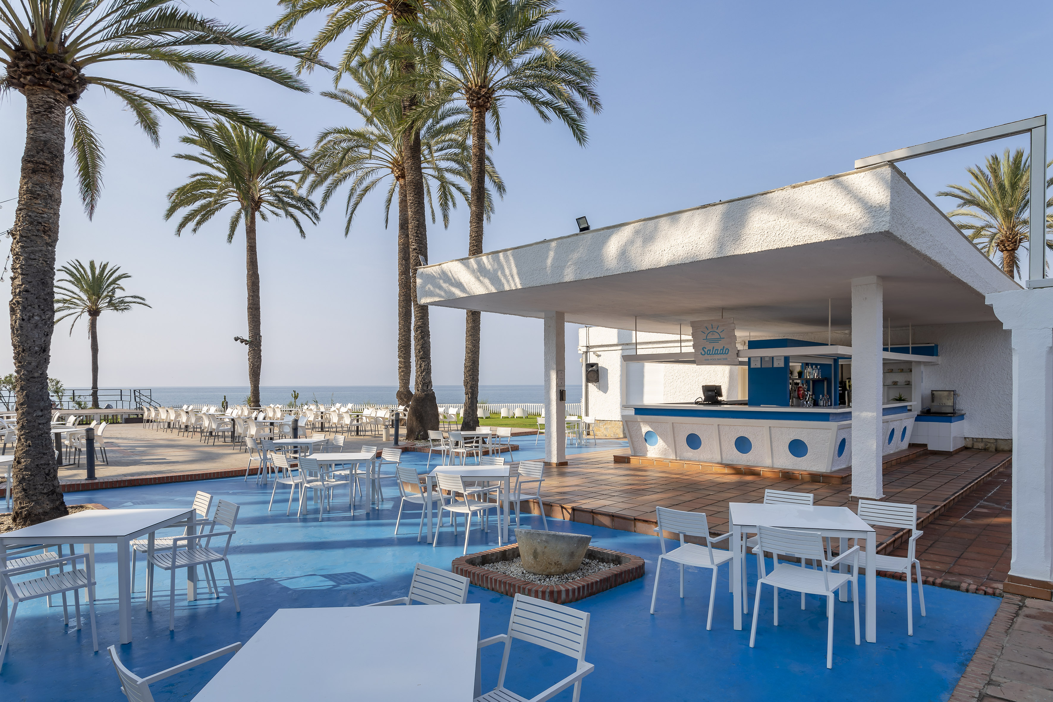 Salado beachfront bar with white tables, blue terrace, palm trees, ocean view.