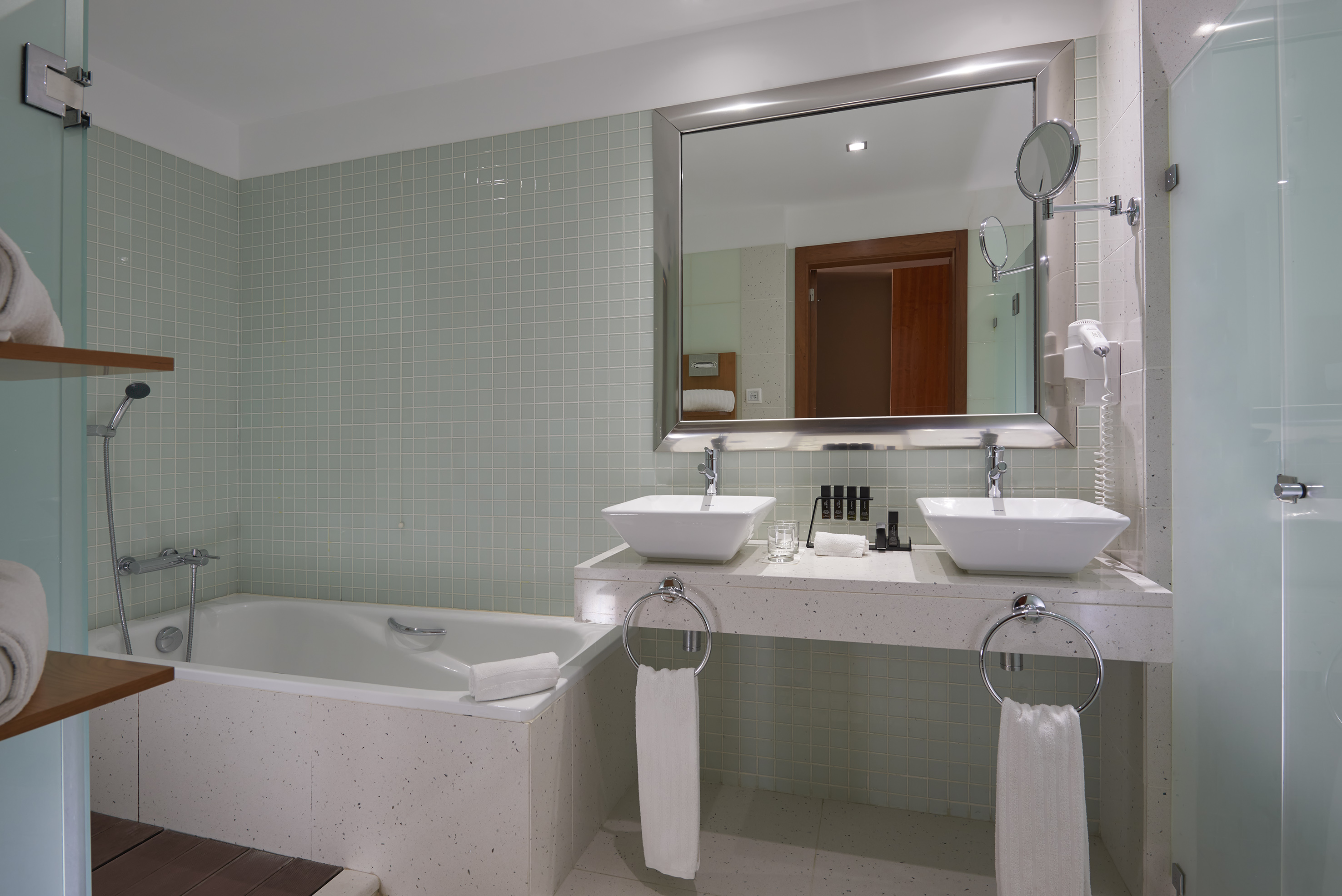 Modern bathroom with light green tiles, double vanity, and bathtub.