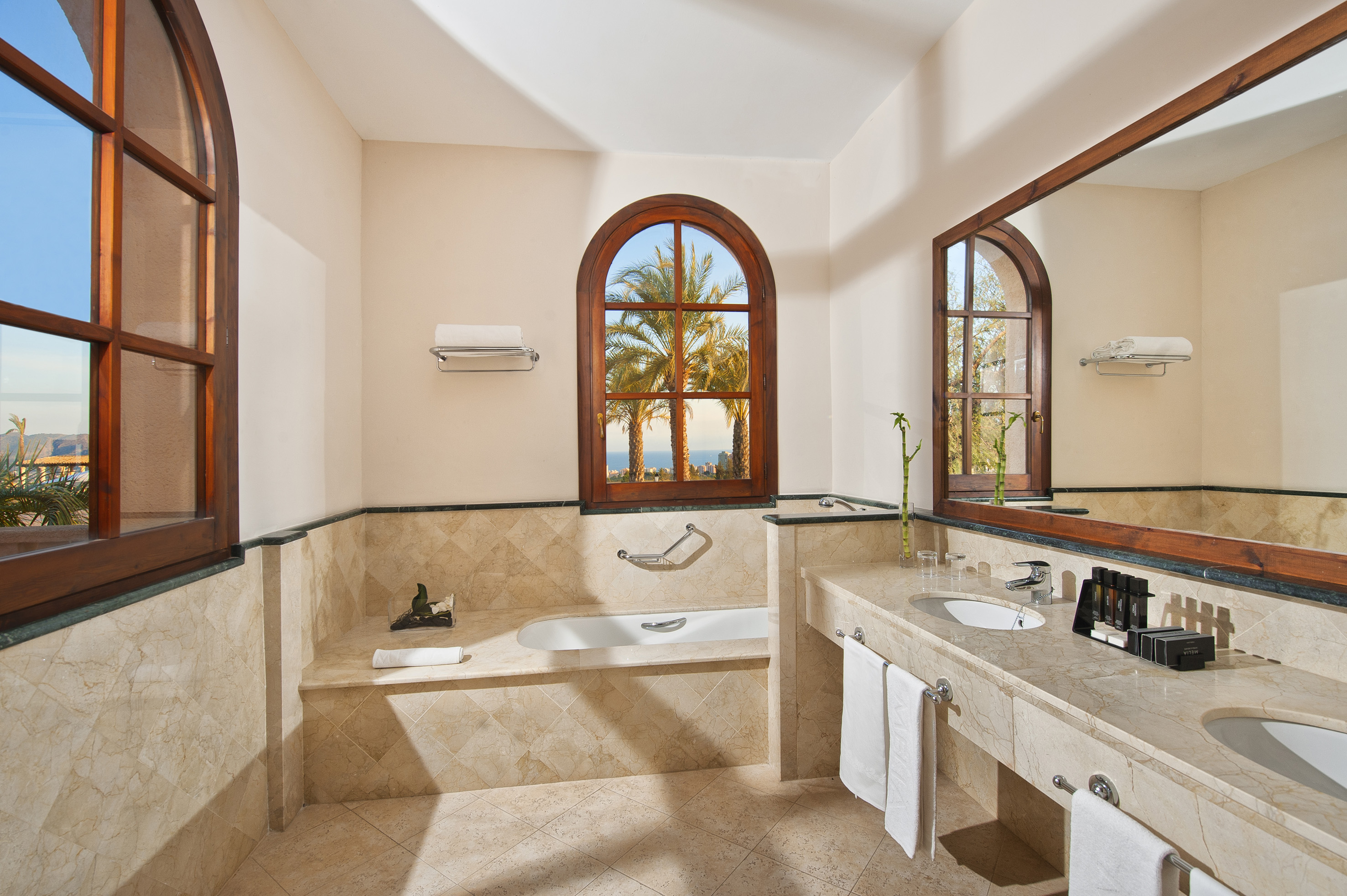 Luxurious marble bathroom with bathtub, double vanity, and palm tree ocean view.