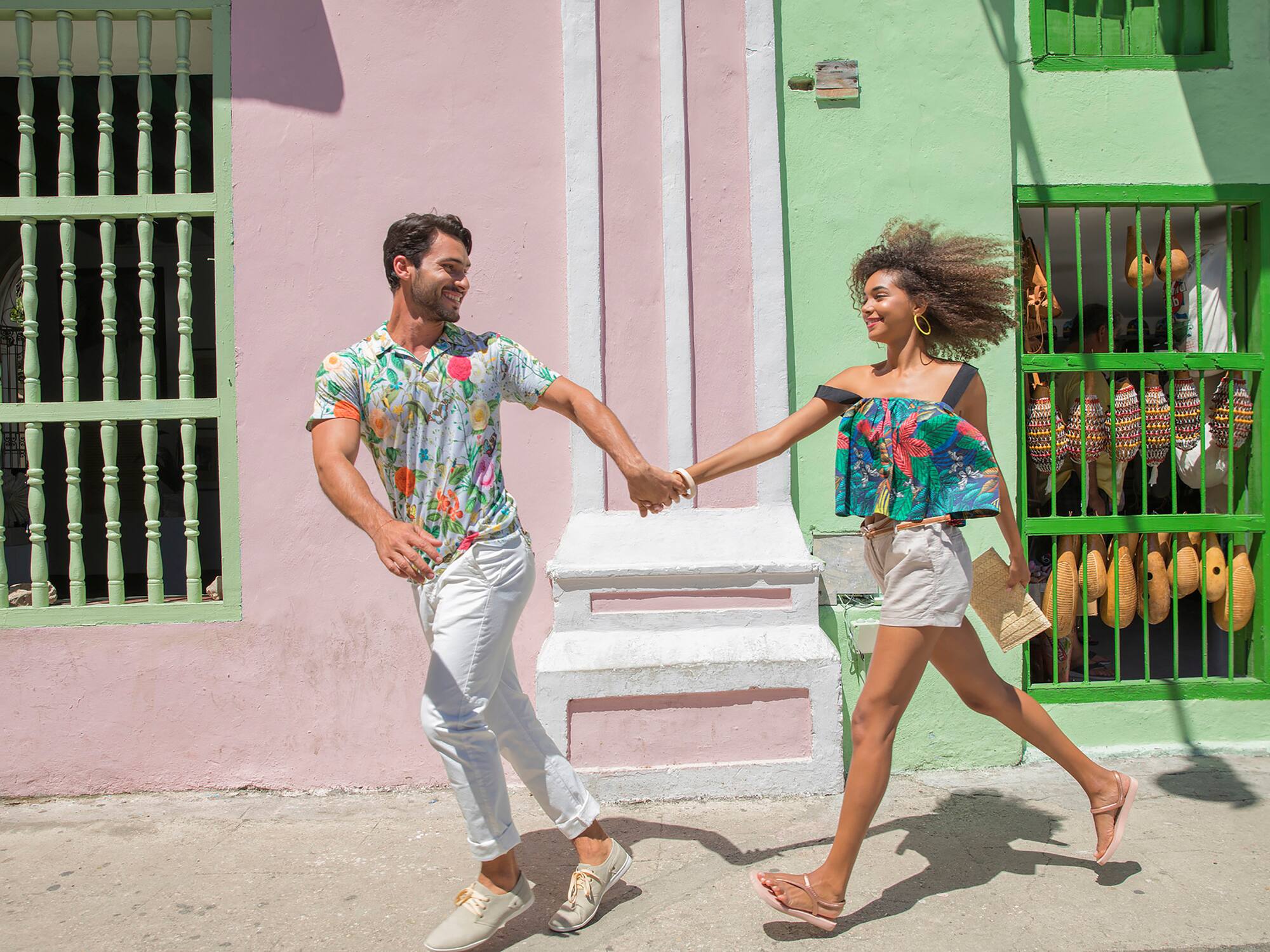 a man and woman holding hands and walking in front of a colorful building