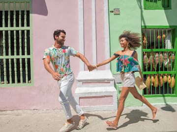 a man and woman holding hands and walking in front of a colorful building
