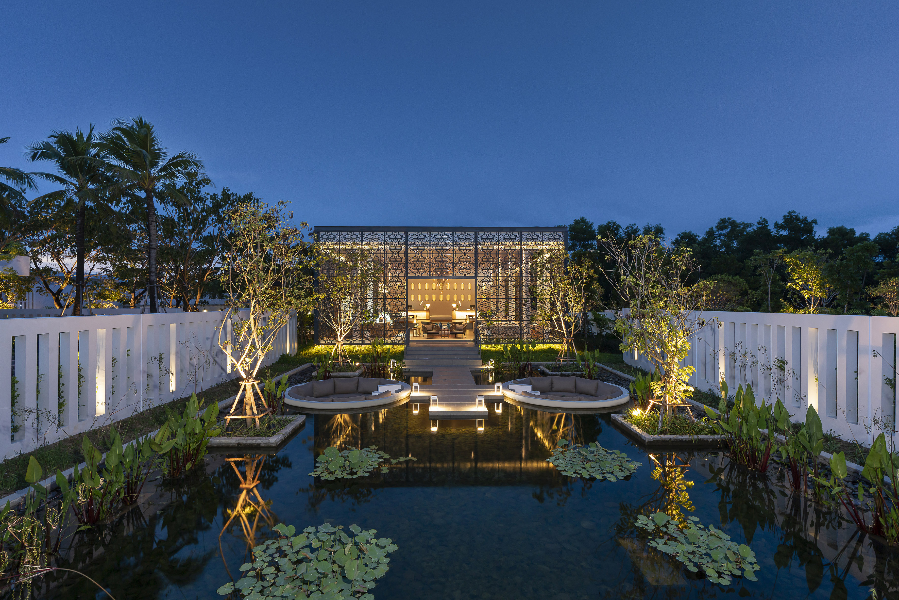 Illuminated modern pavilion, reflecting pond, and outdoor lounge seating at dusk.