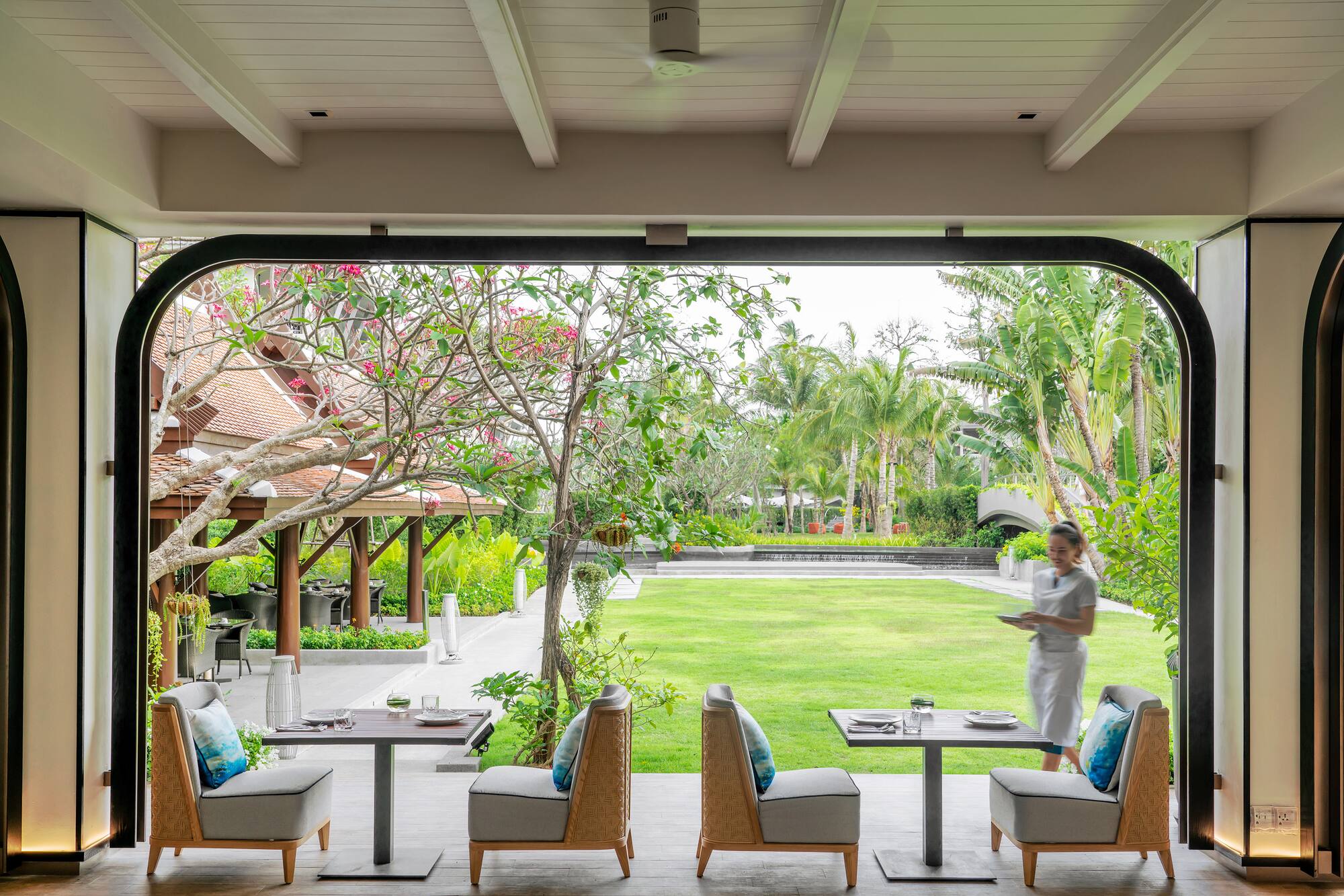 Tropical resort outdoor dining with garden view and staff.