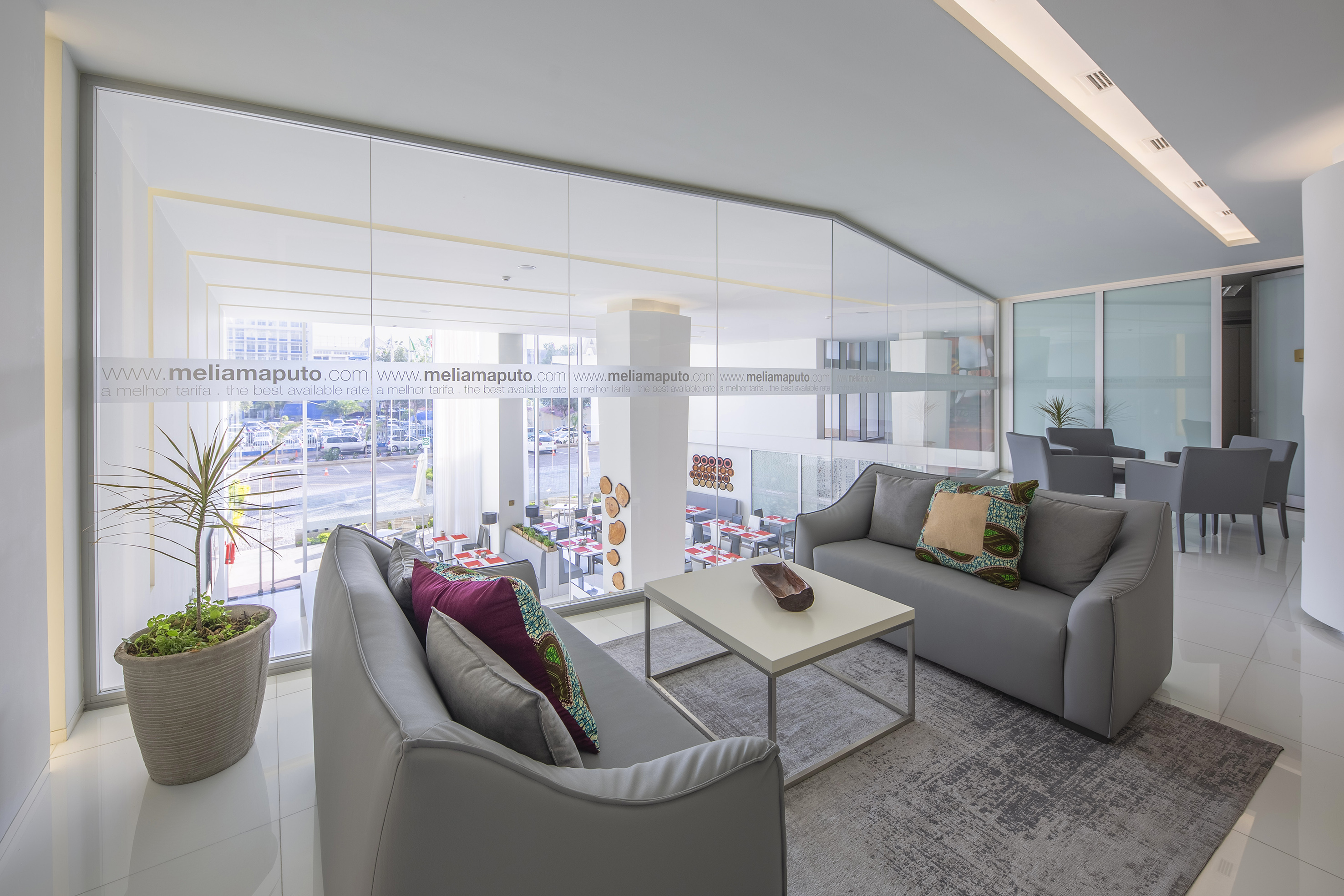 Meliá Maputo hotel lounge with grey sofas, glass walls, and restaurant view.