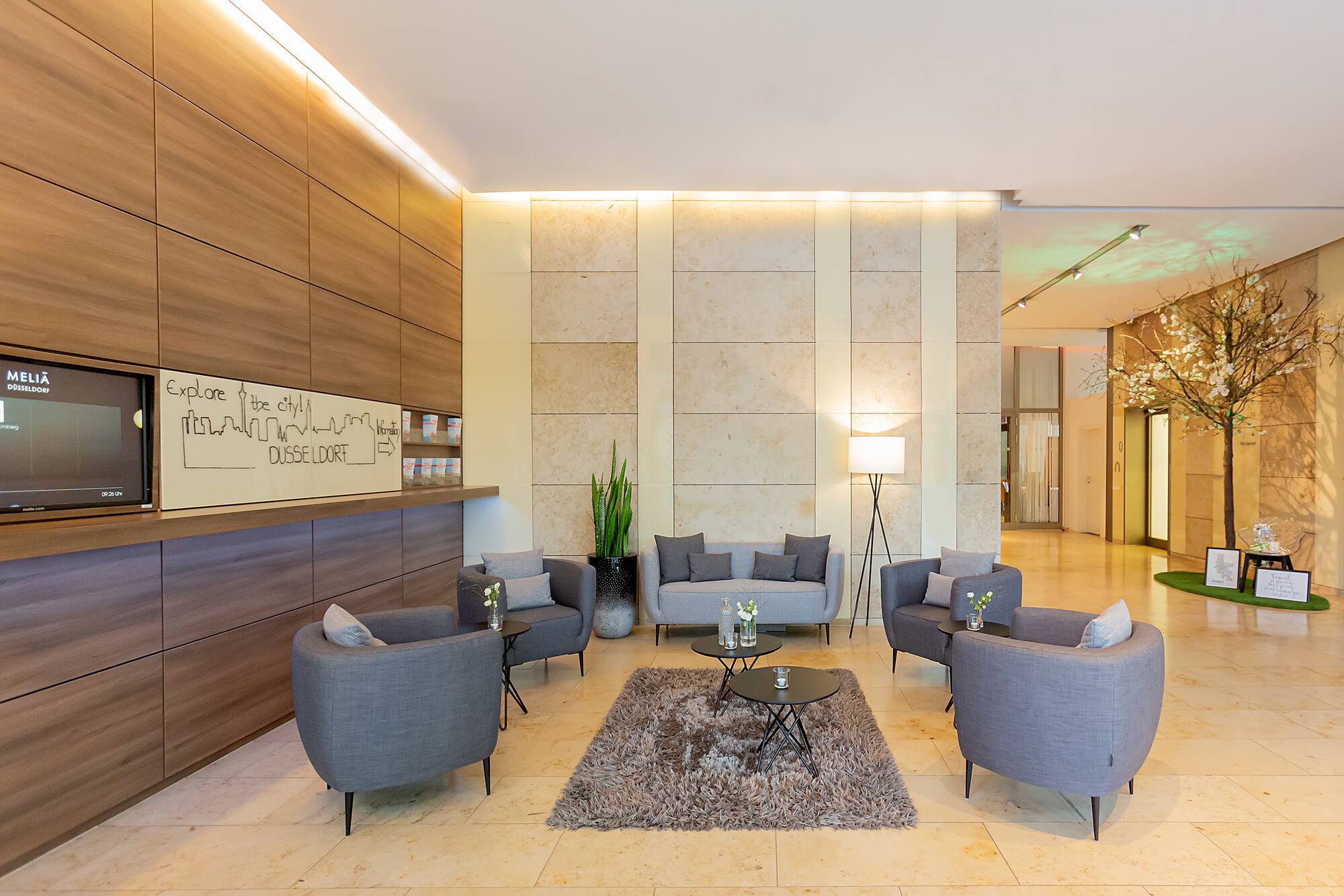 Meliá Düsseldorf hotel lobby with modern grey lounge seating, rug, and wood reception.