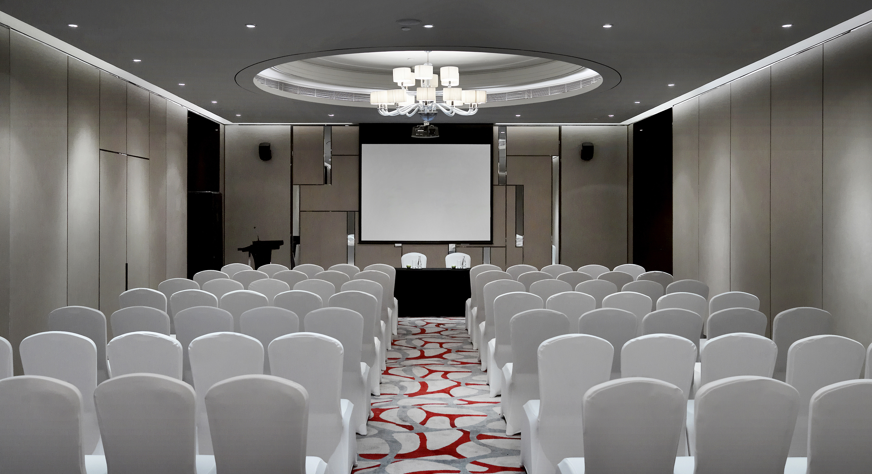 Empty conference room with white chairs, projector screen, and modern decor.