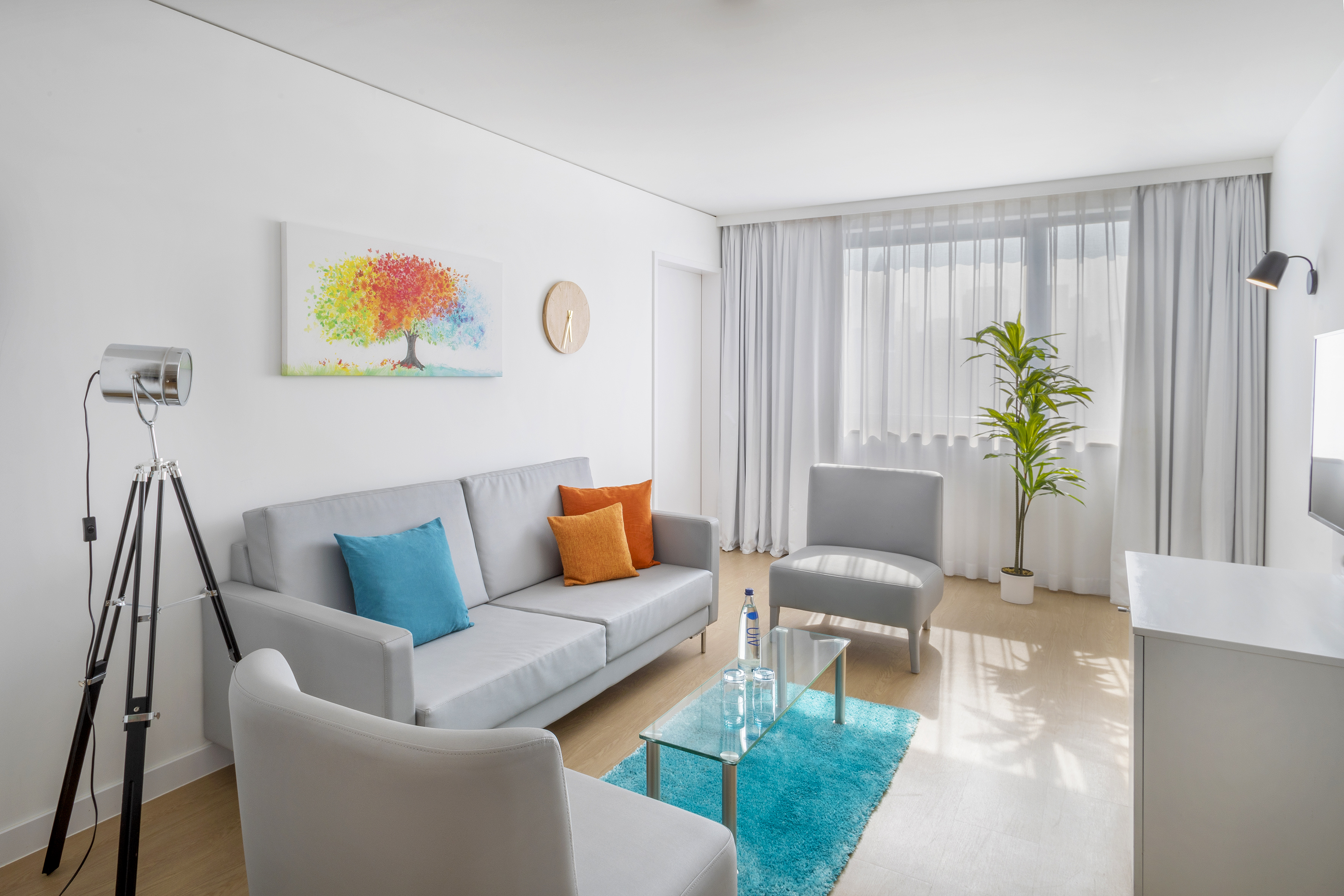 Bright modern living room with grey sofa, colorful painting, and turquoise rug.