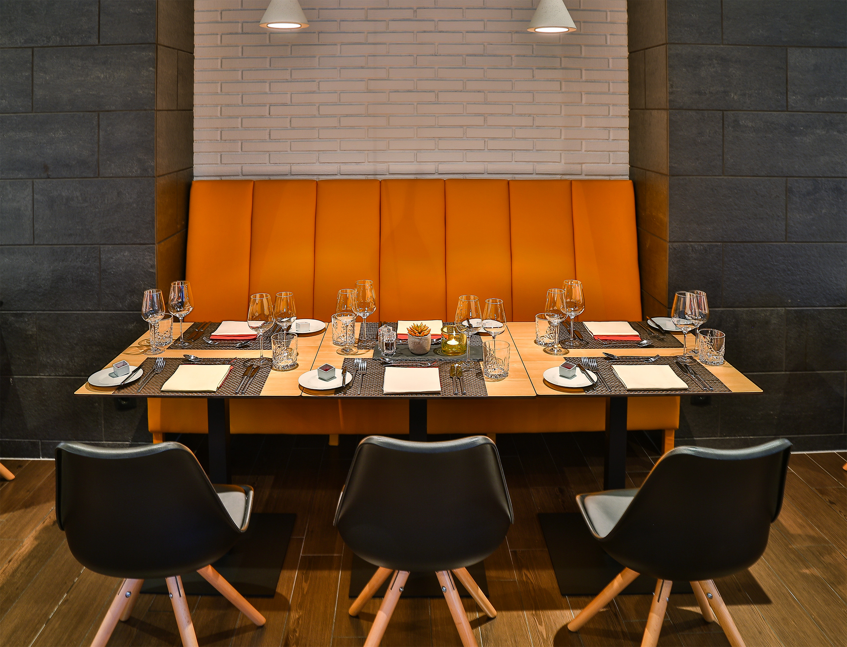Elegant restaurant dining table with orange booth, modern chairs, and brick wall.