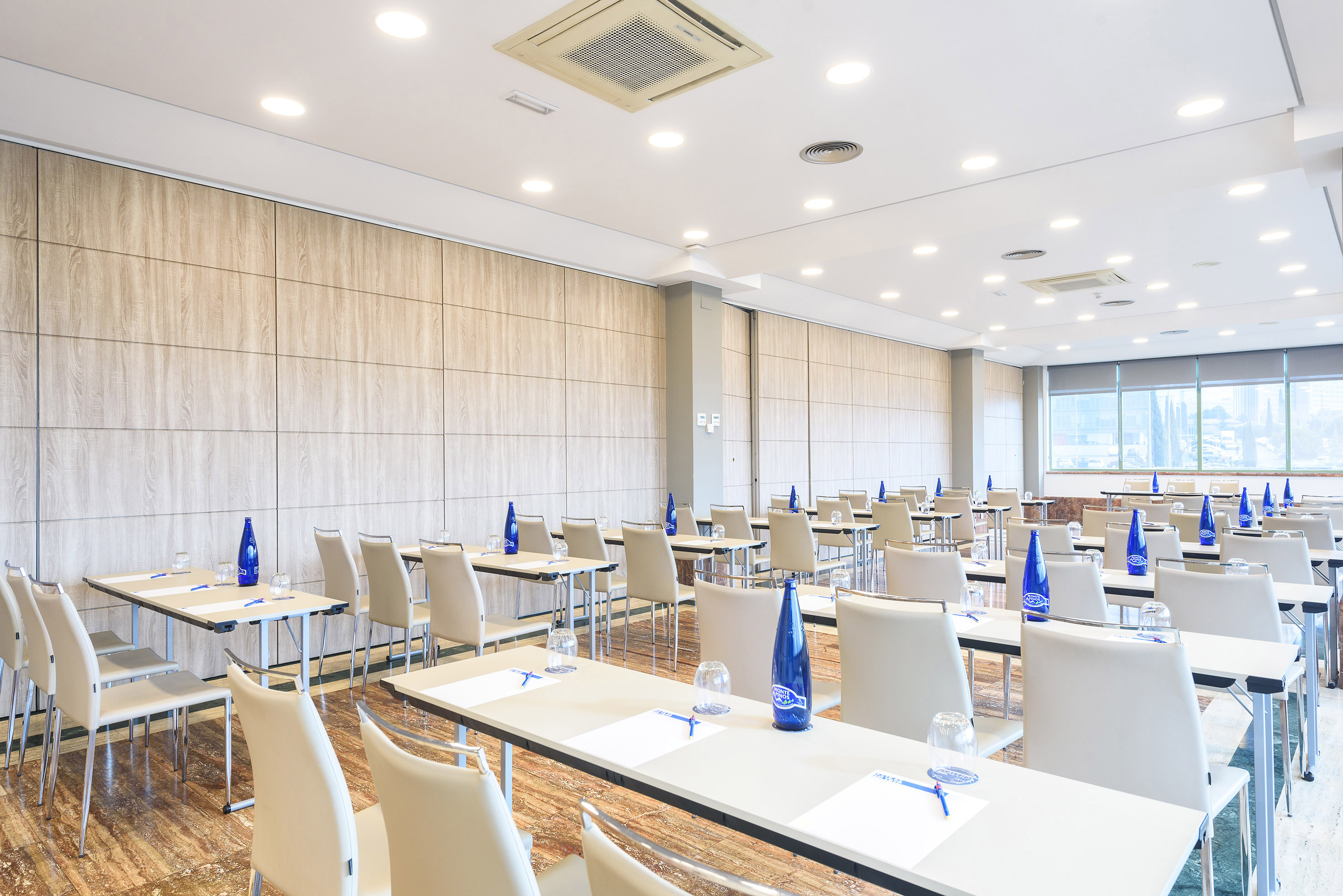 Contemporary conference room setup with rows of tables, chairs, bottled water.