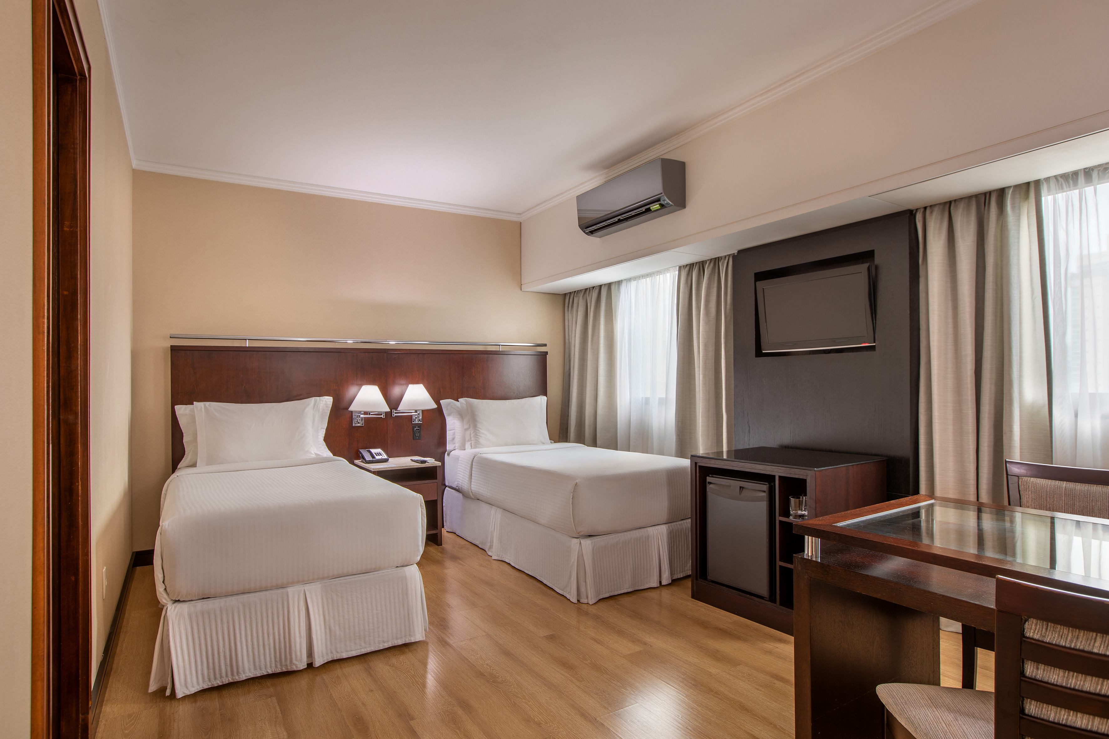 Hotel room: two twin beds, wooden floor, flat-screen TV, desk, mini-fridge.