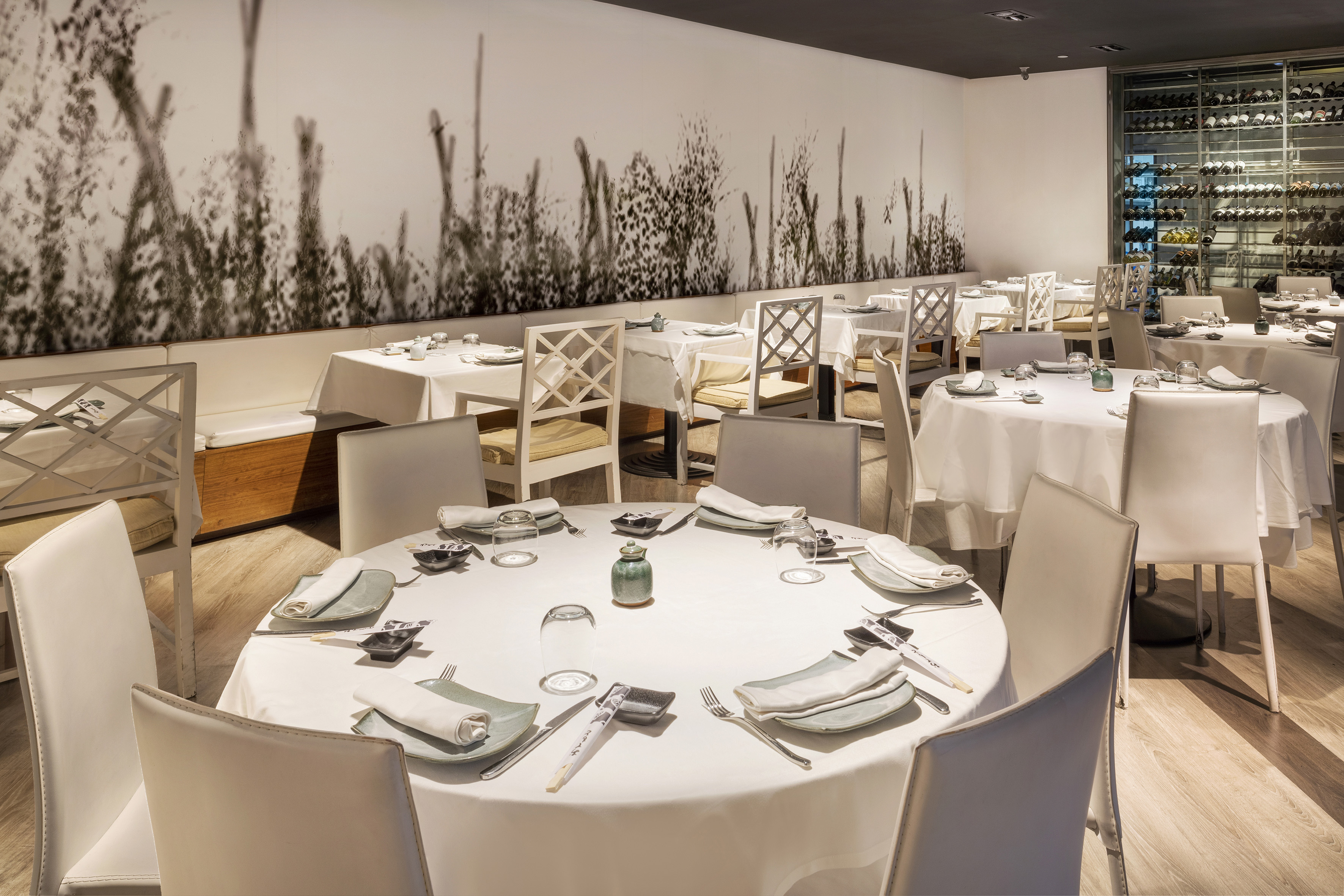 Elegant restaurant dining room with white tables, minimalist decor, and a wine wall.