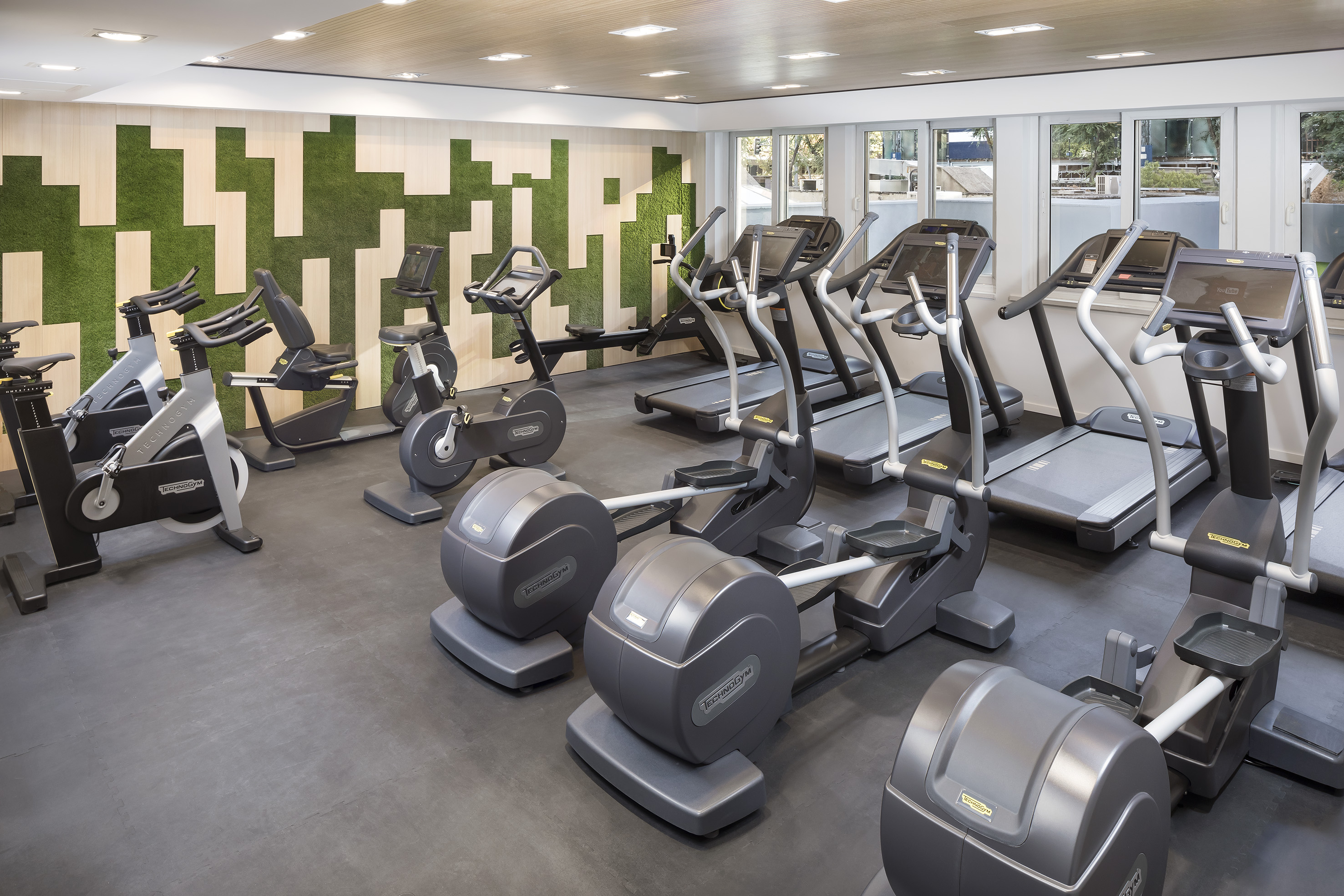 Modern gym: Technogym treadmills, ellipticals, bikes, green accent wall.