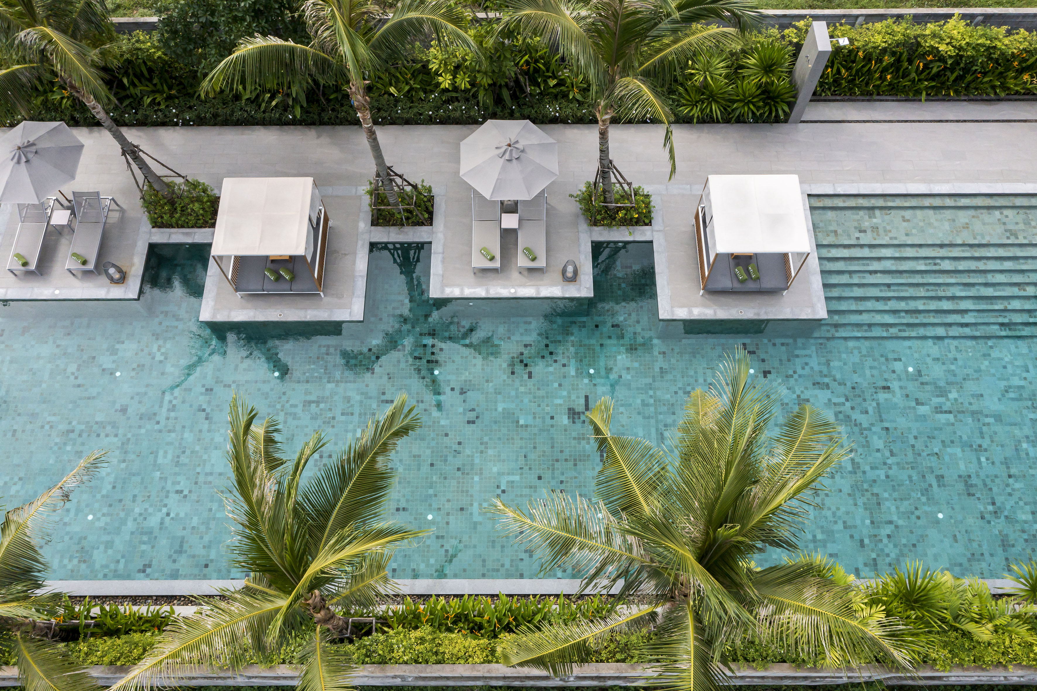 Aerial view: luxury resort pool, palm trees, sun loungers, private cabanas.