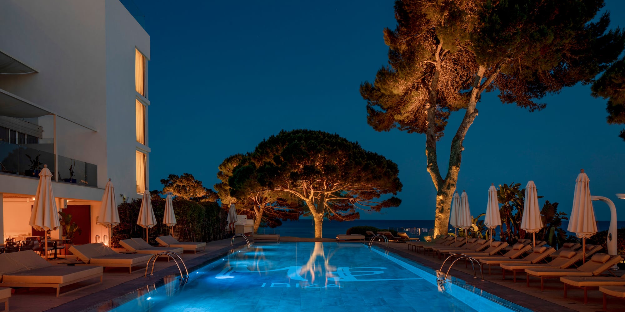 a pool with trees and chairs and a building at night