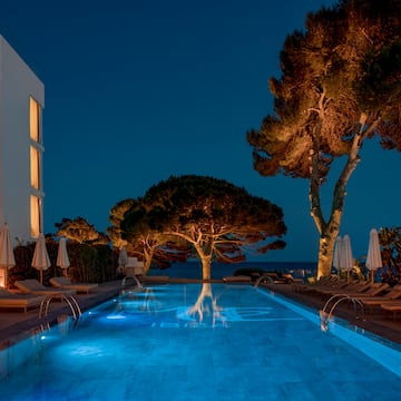a pool with trees and chairs and a building at night