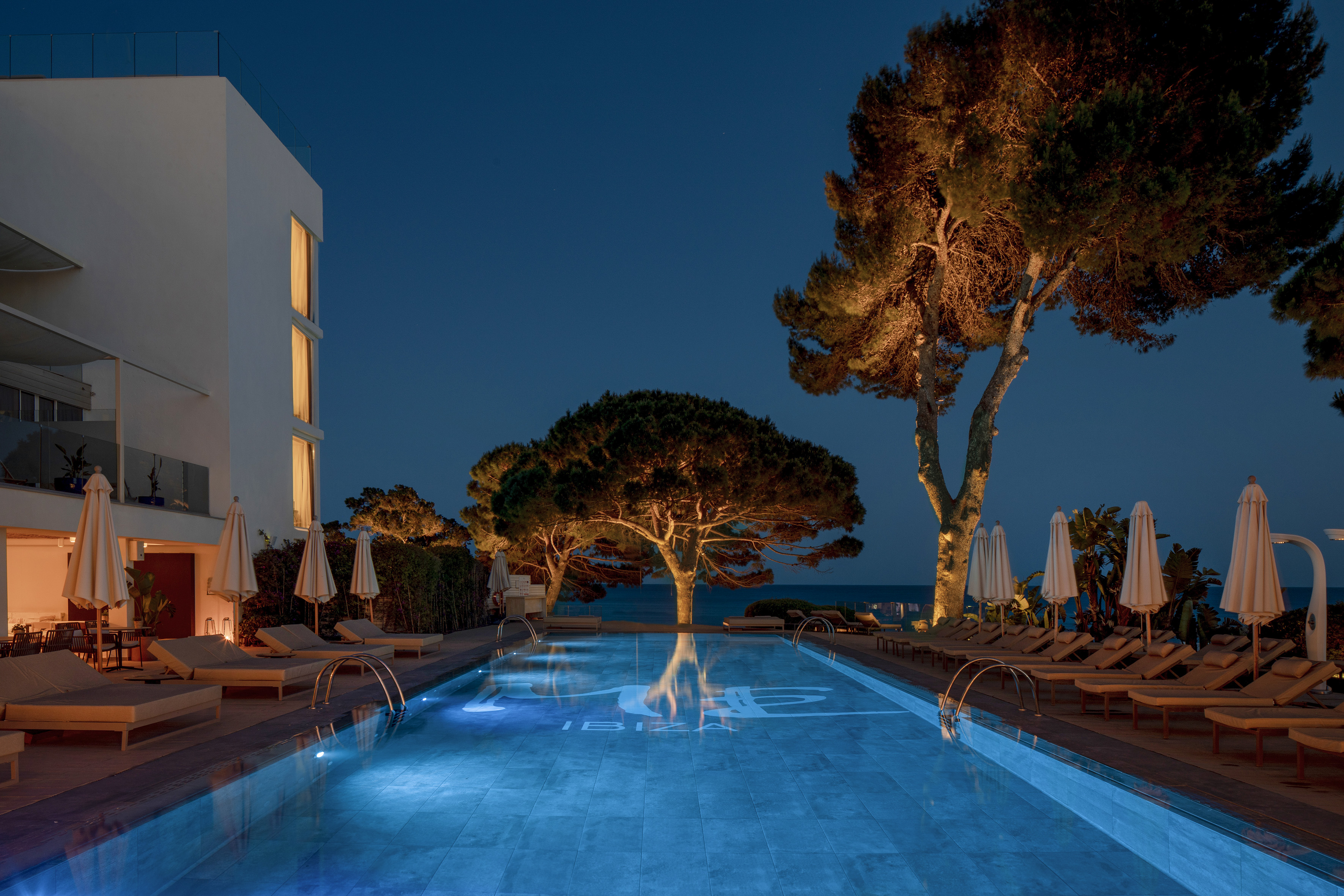 a pool with trees and chairs and a building at night