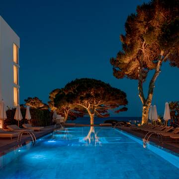 a pool with trees and chairs and a building at night