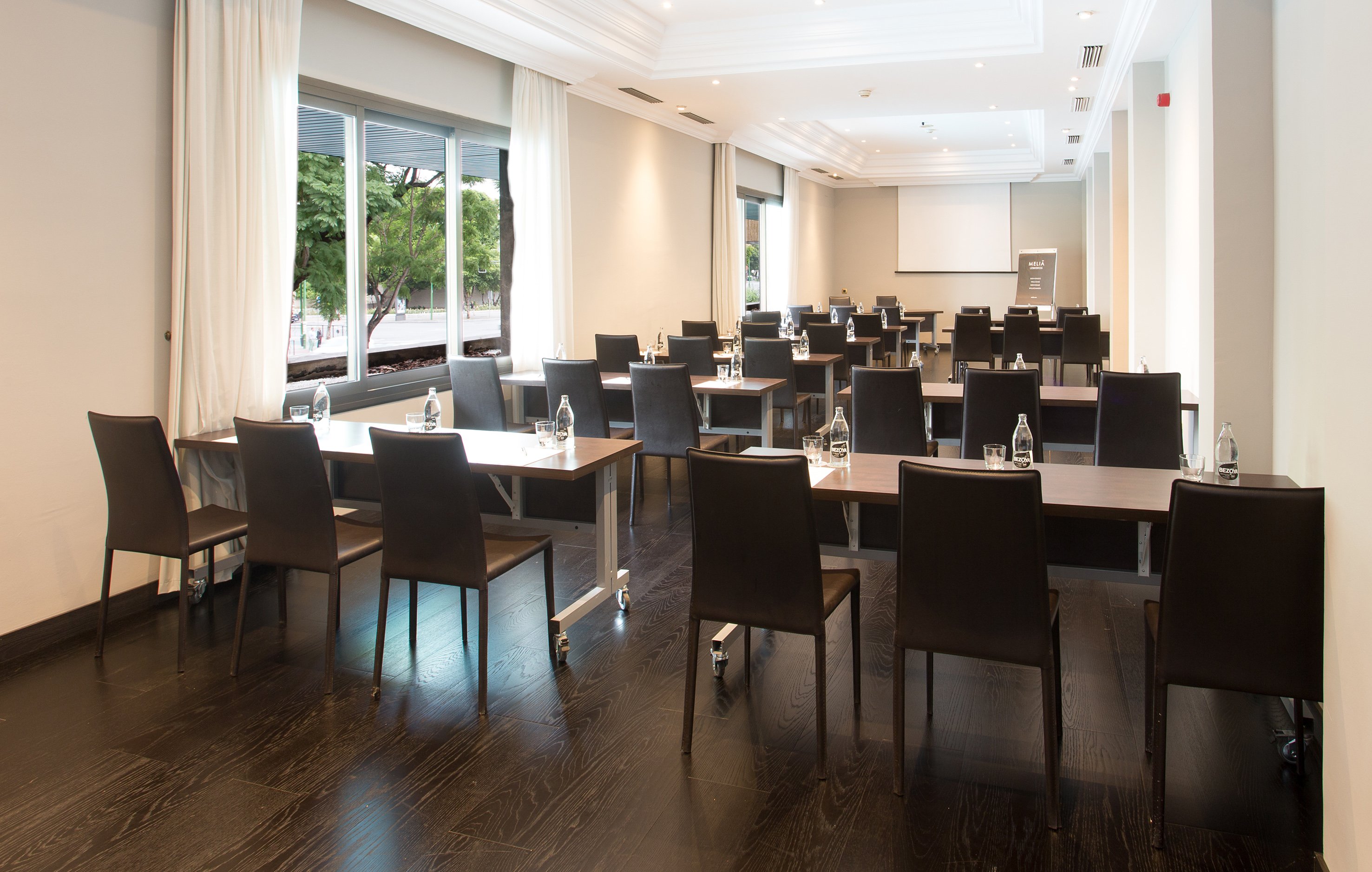 Modern conference room with projector screen, tables, chairs, and large windows.