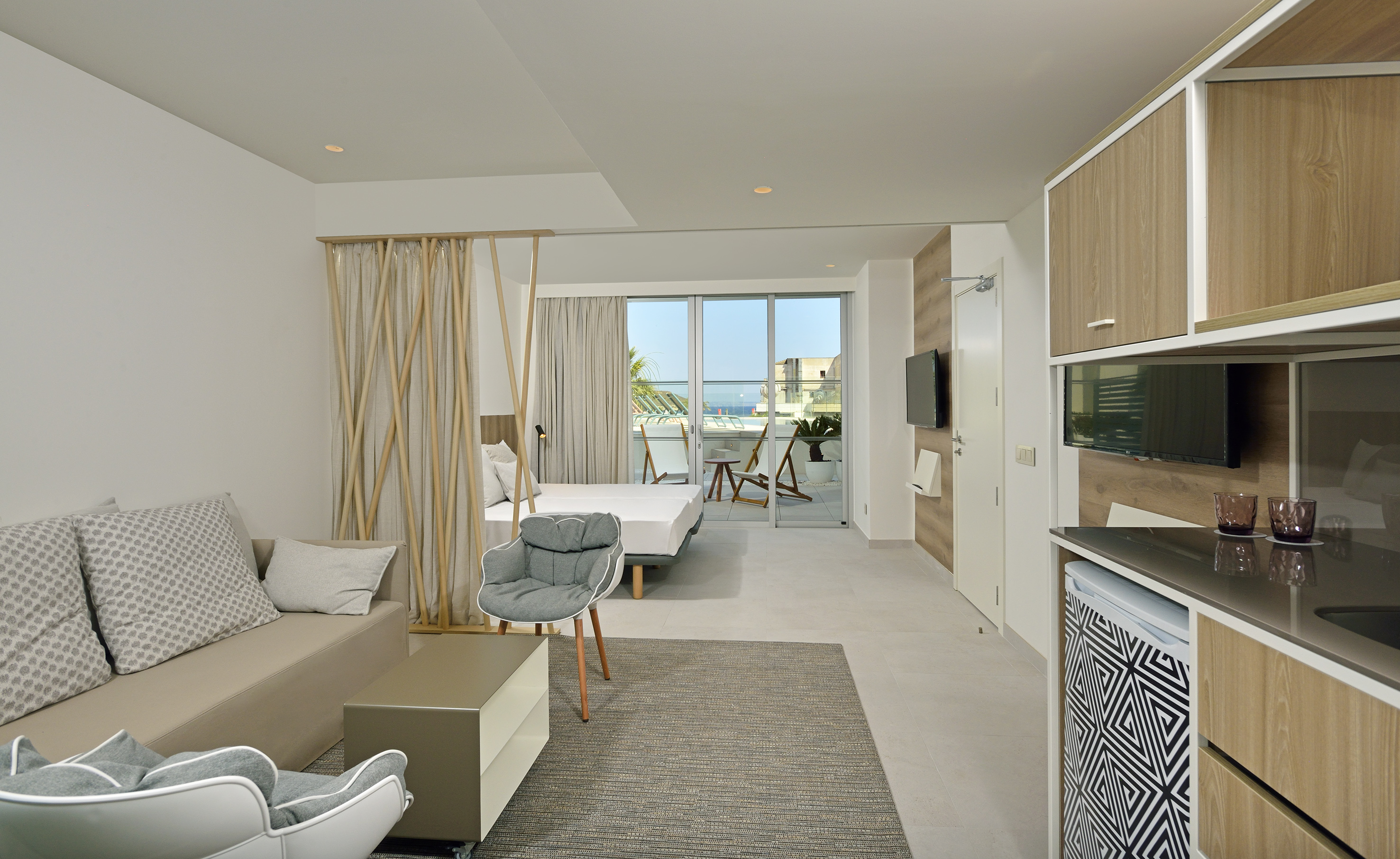Modern studio with bed, sofa, kitchenette, and balcony with sea view.