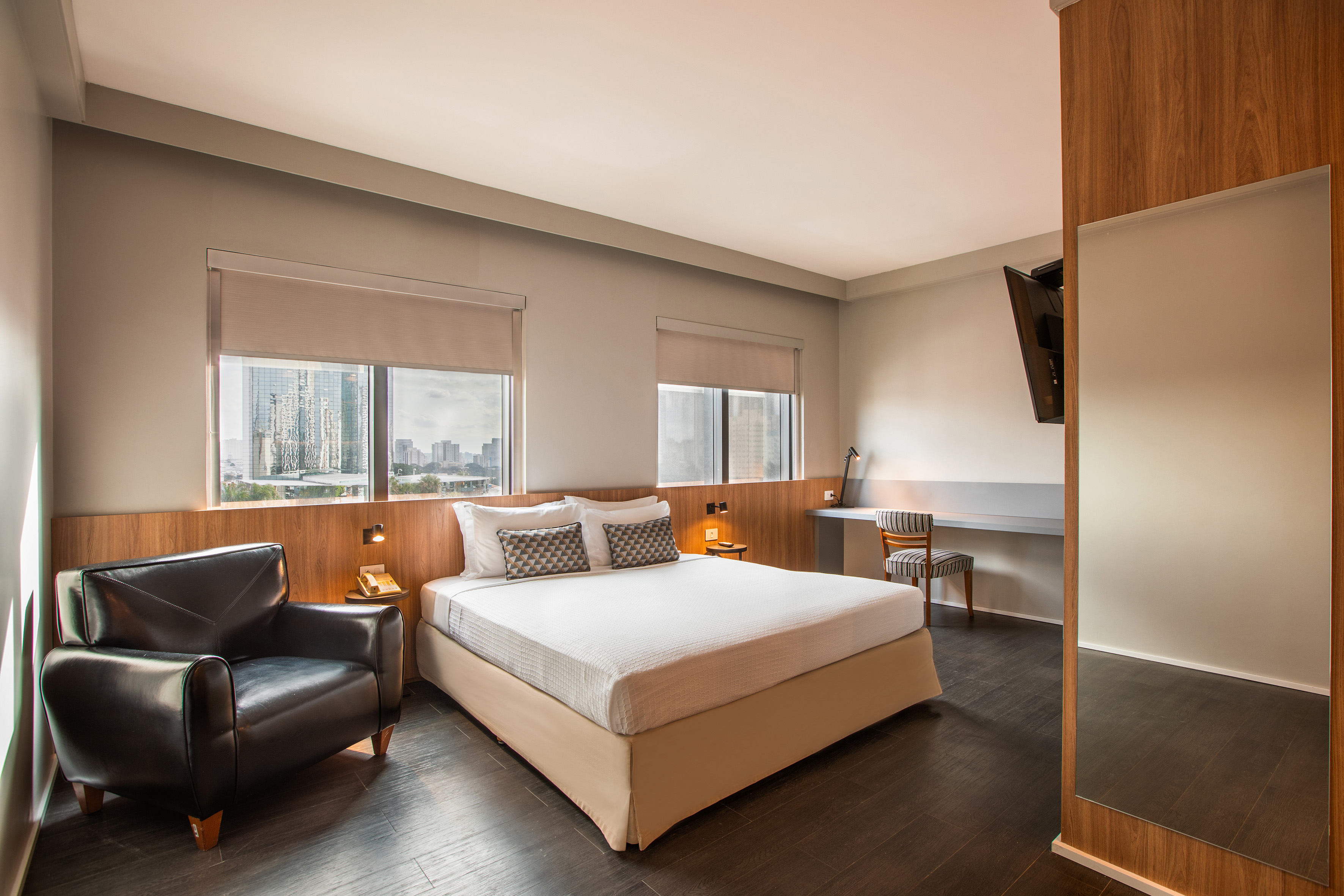 Modern hotel room with king bed, city view, leather armchair, and desk.