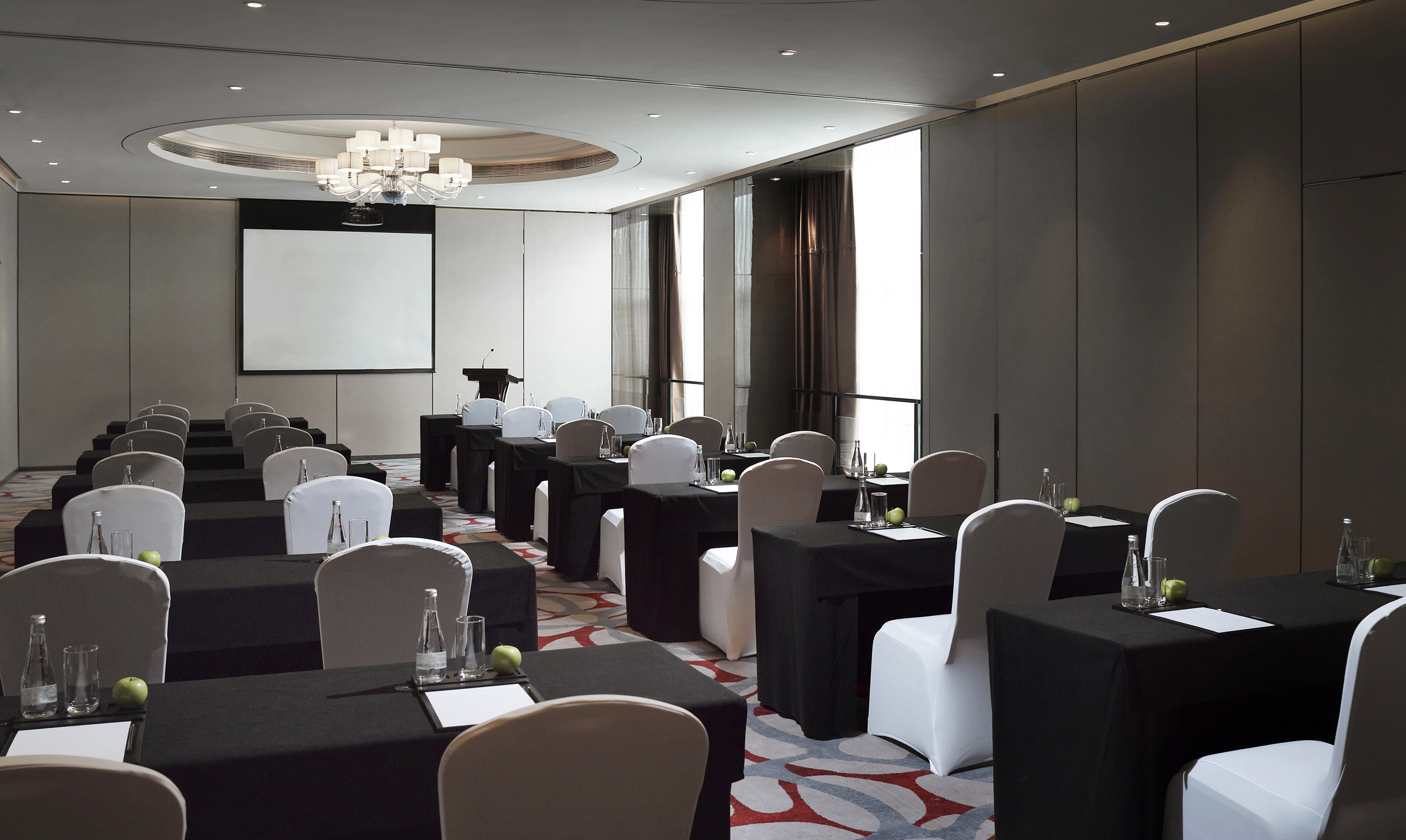 Modern corporate meeting room with tables, chairs, screen, and lectern.