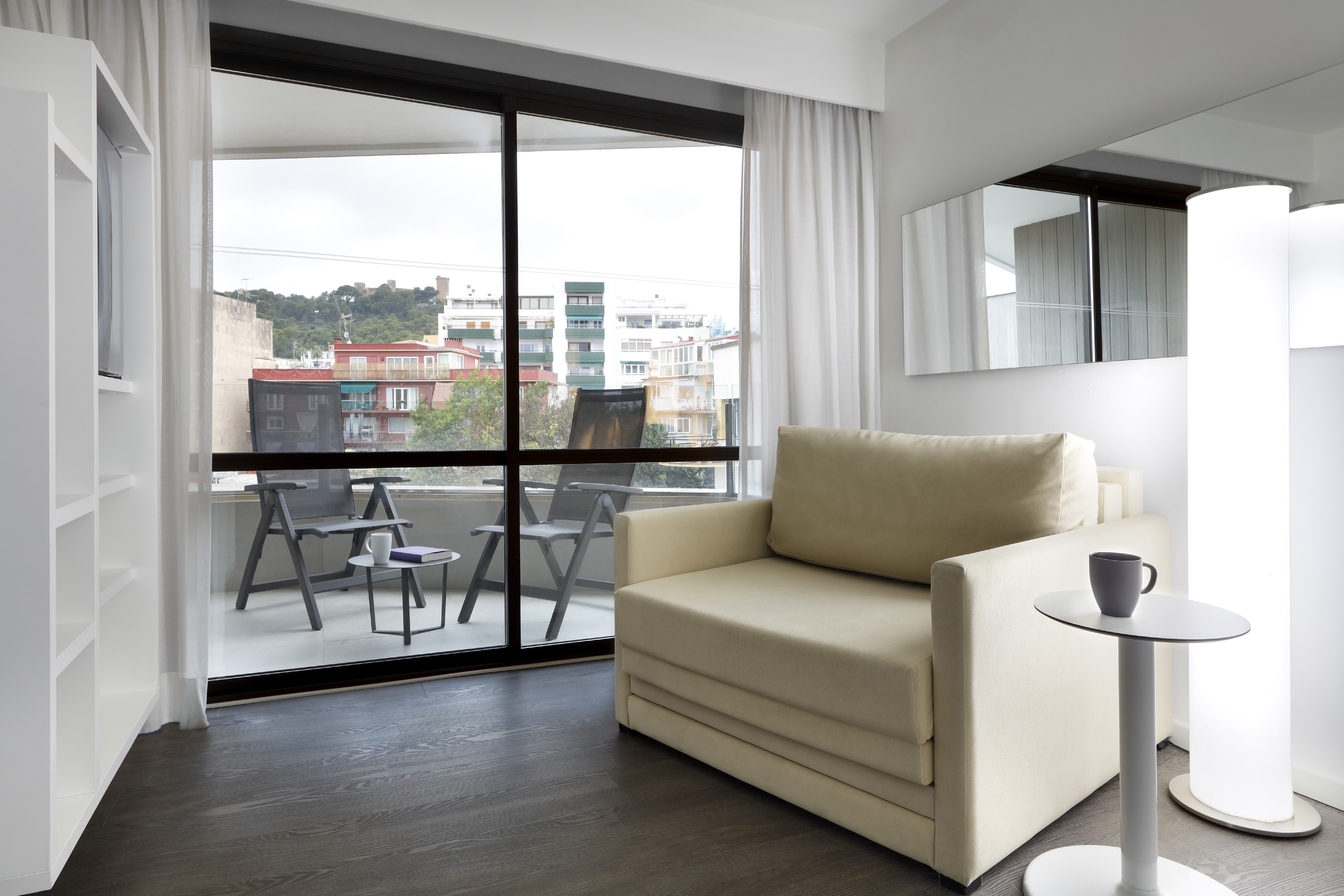 Modern hotel living area with cream sofa, balcony, and city mountain view.