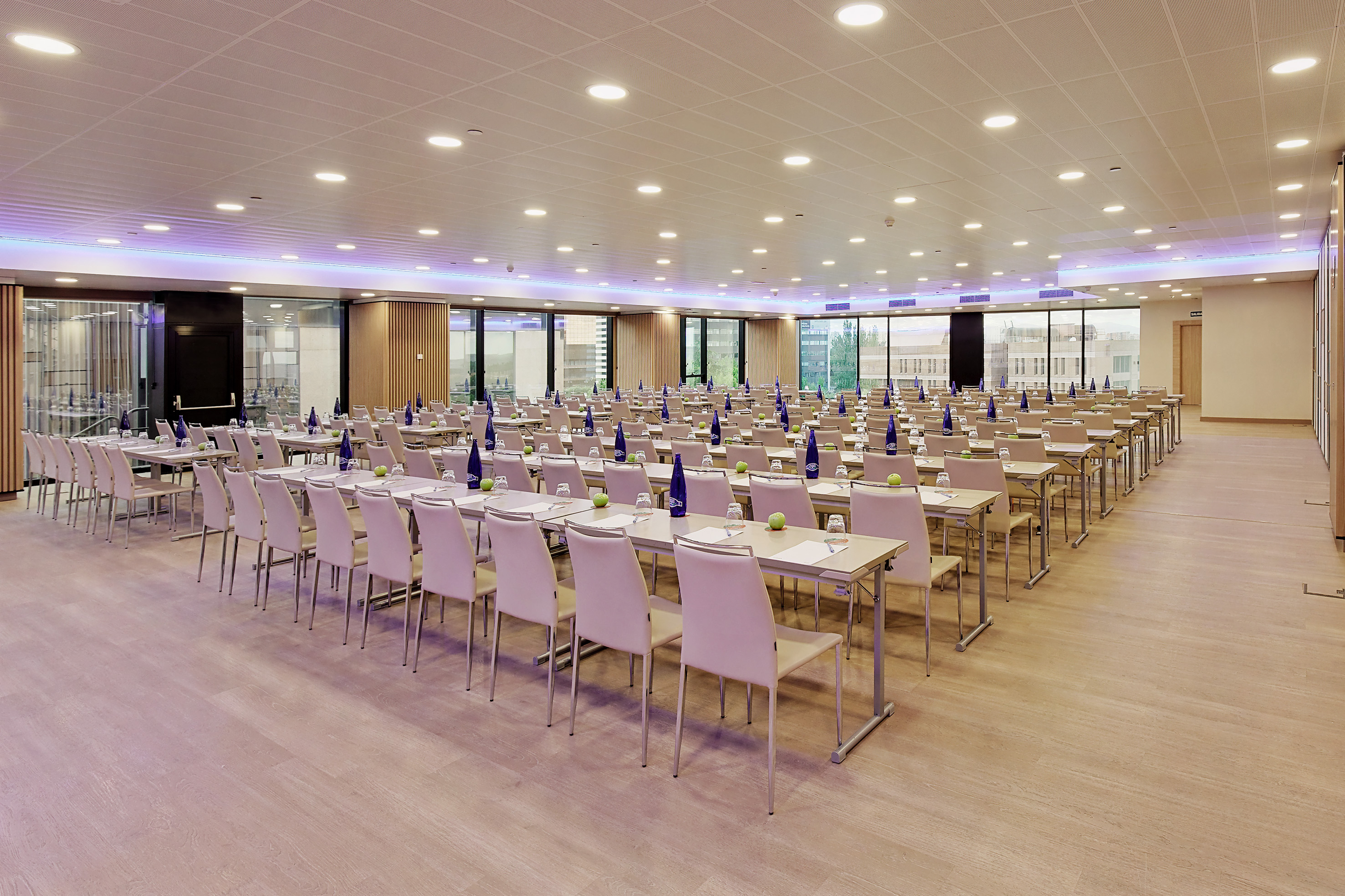 Modern conference room with tables, chairs, water bottles, and large windows.